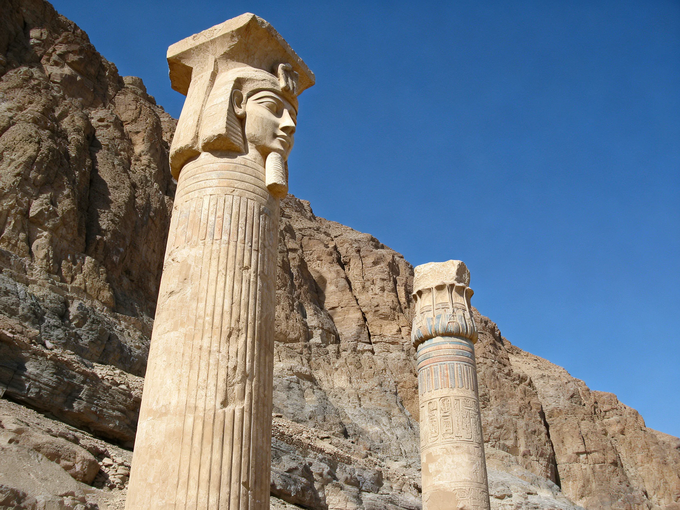 Two ancient stone columns stand against rocky cliffs under clear blue sky