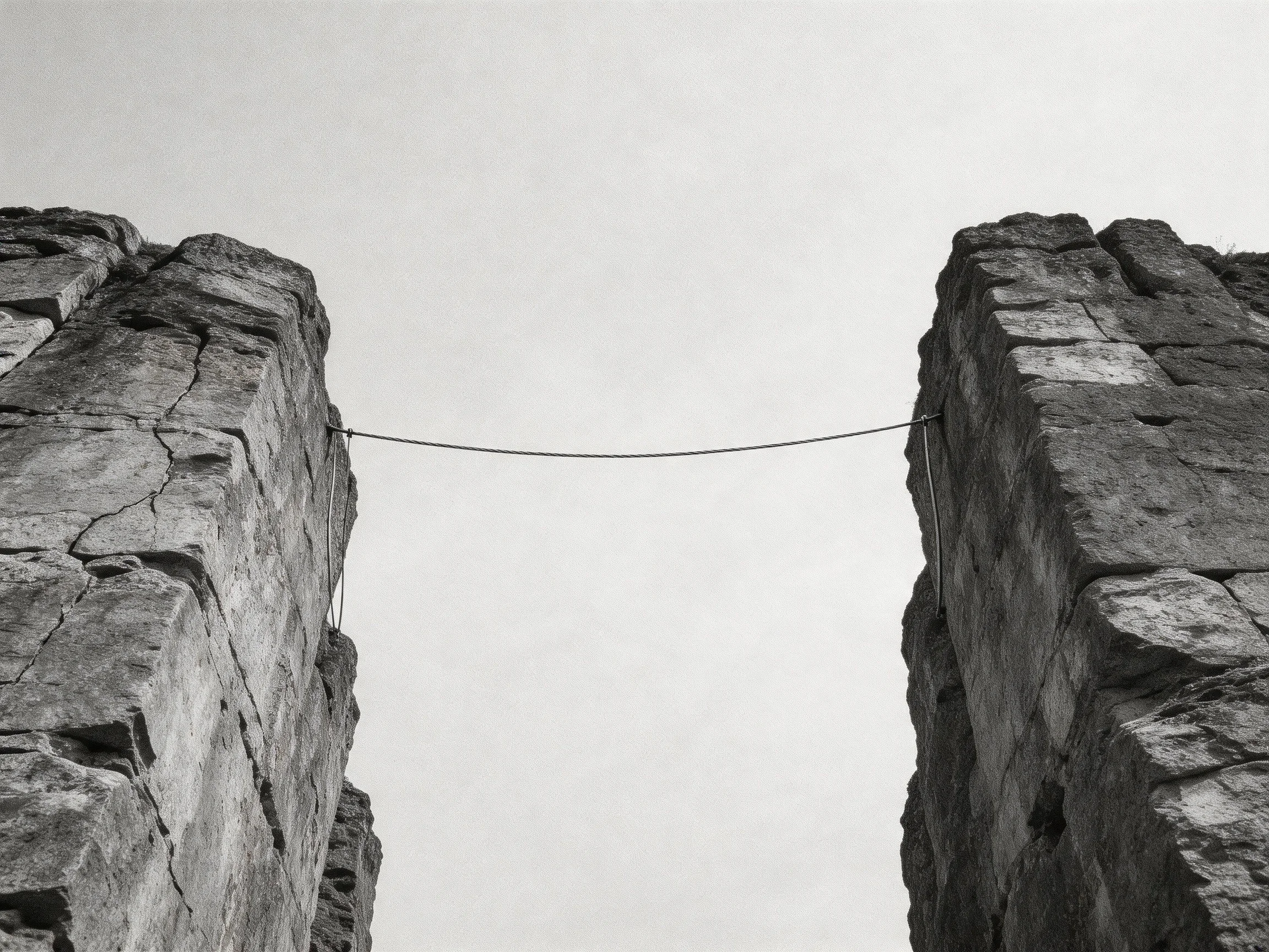 Two ancient stone towers connected by a thin wire under an overcast sky
