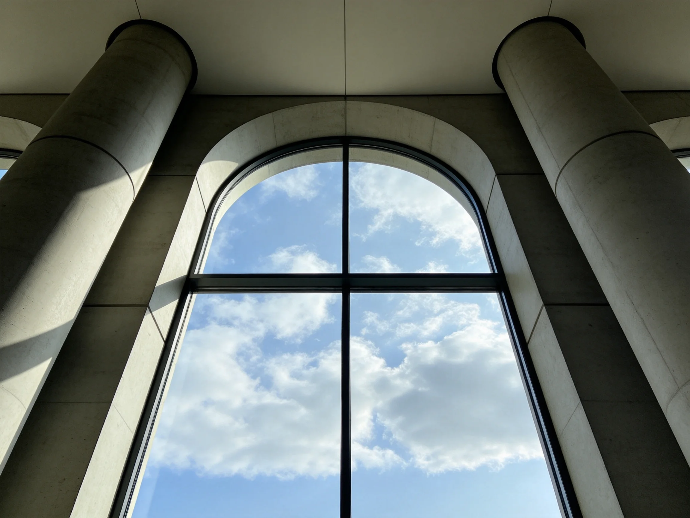 Two large concrete columns frame an arched window with blue sky and white clouds