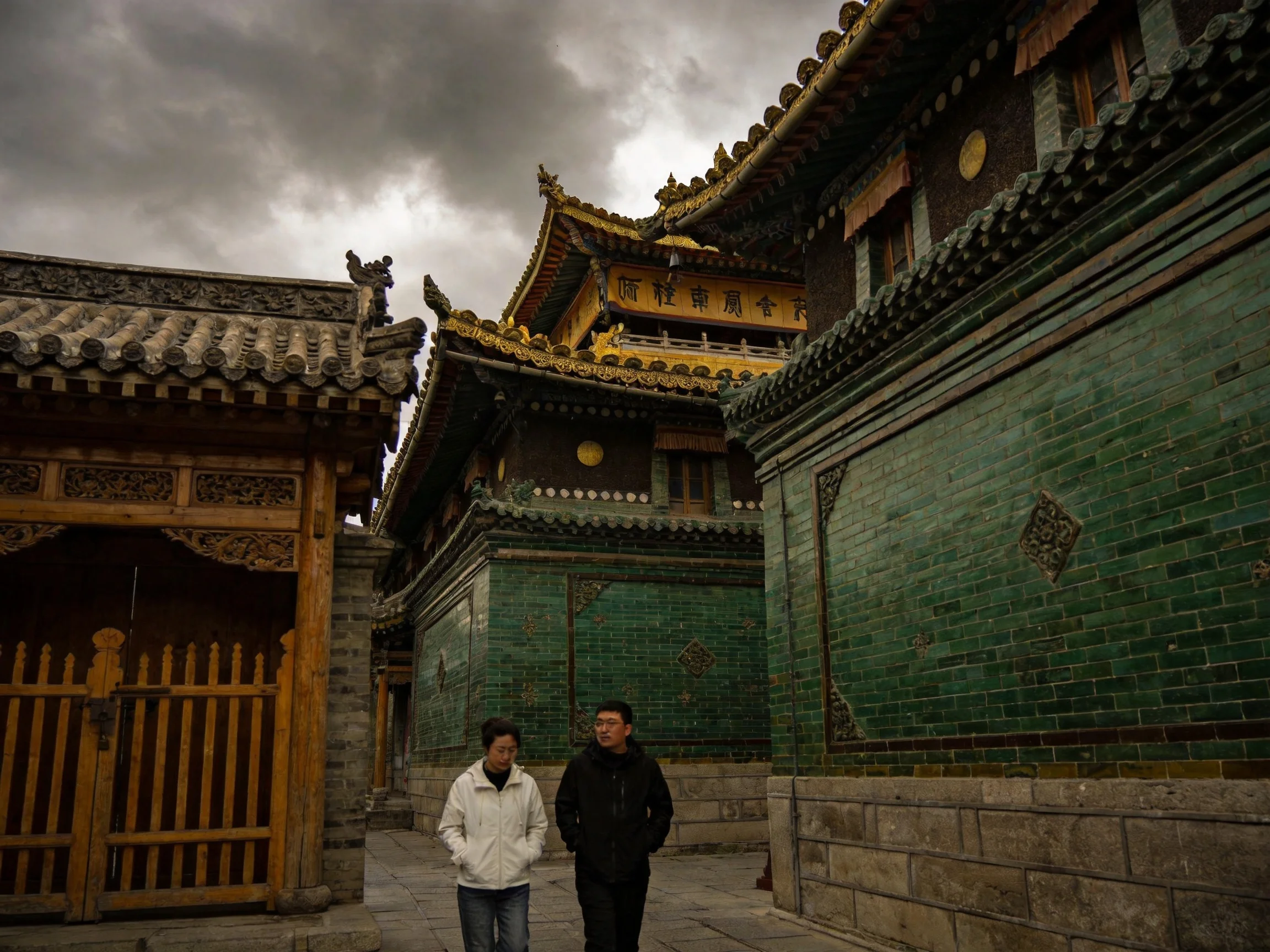 Two people walk near ancient temples with green brick walls and golden roofs