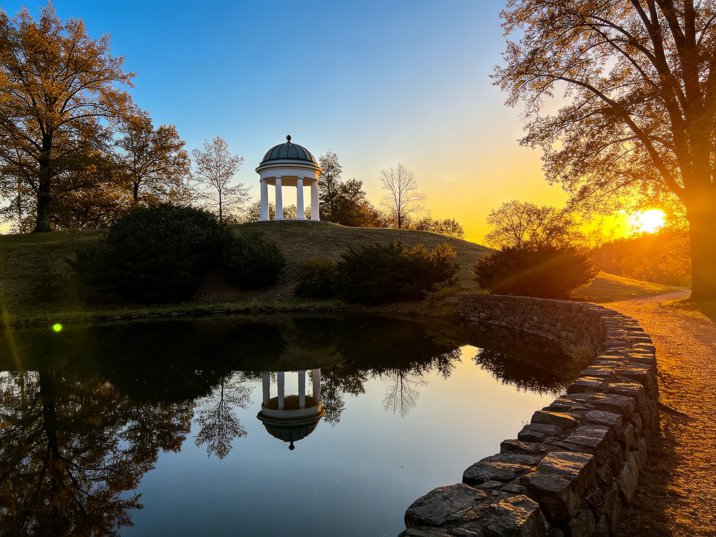 White gazebo reflected in pond near stone path at golden sunset