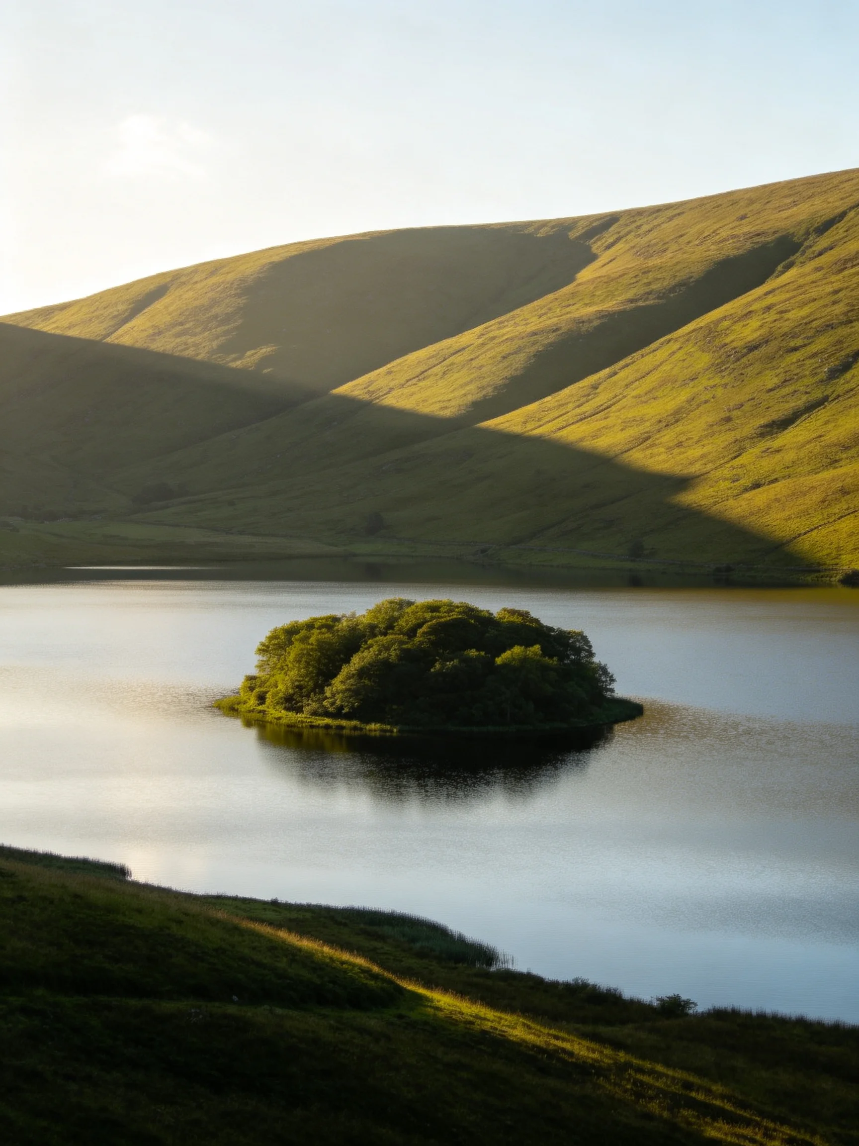 A serene lake with a lush central island and rolling green hills