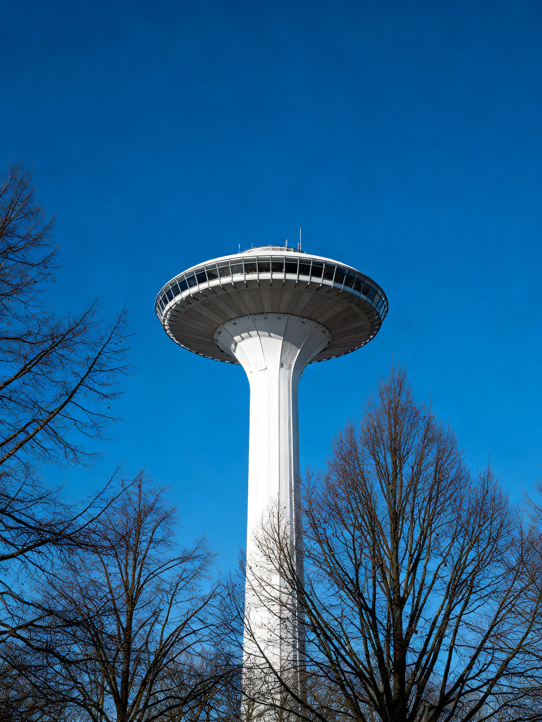 A tall white observation tower with circular deck under clear blue sky