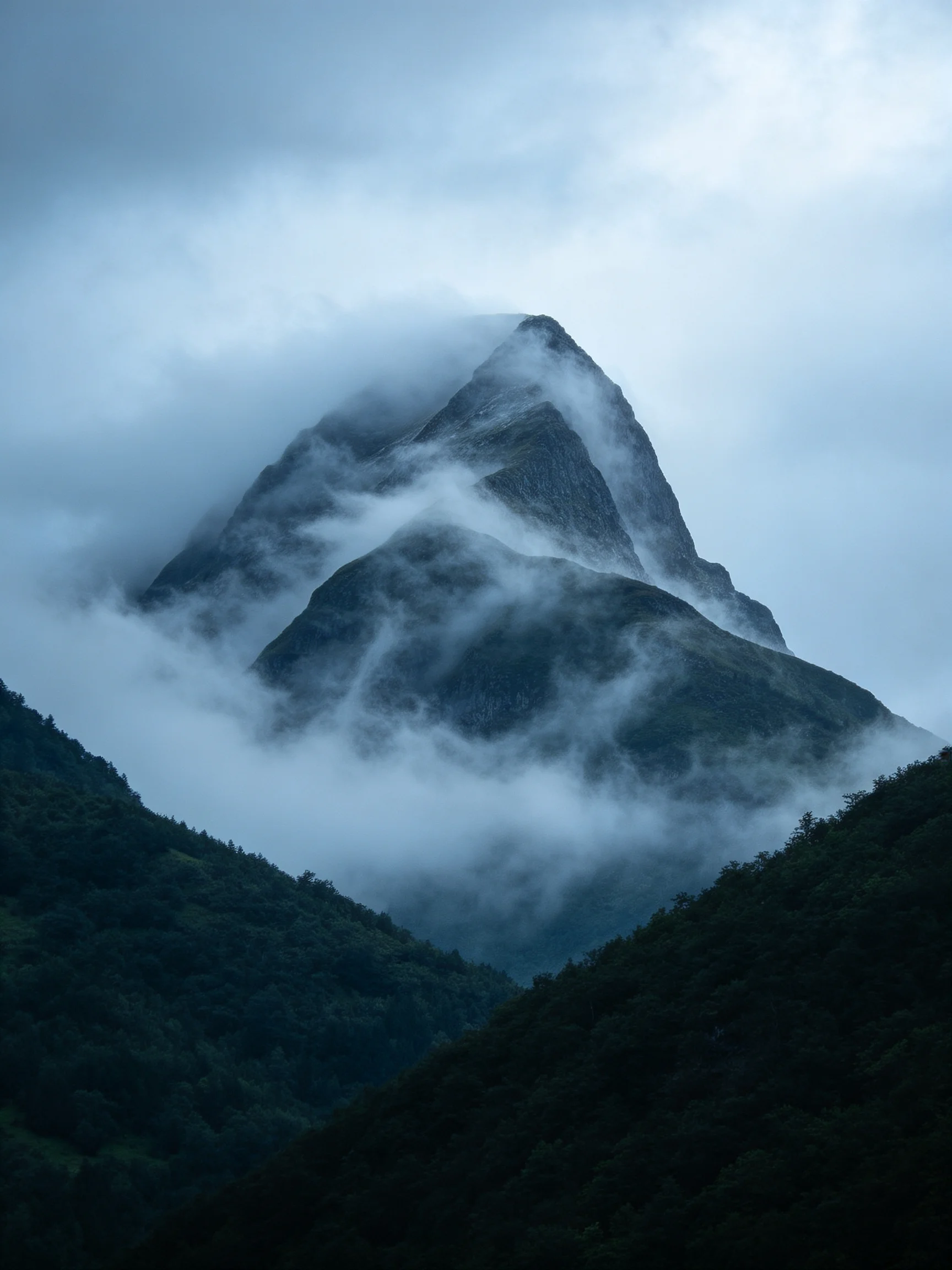 A towering mountain shrouded in misty clouds over dark green forests