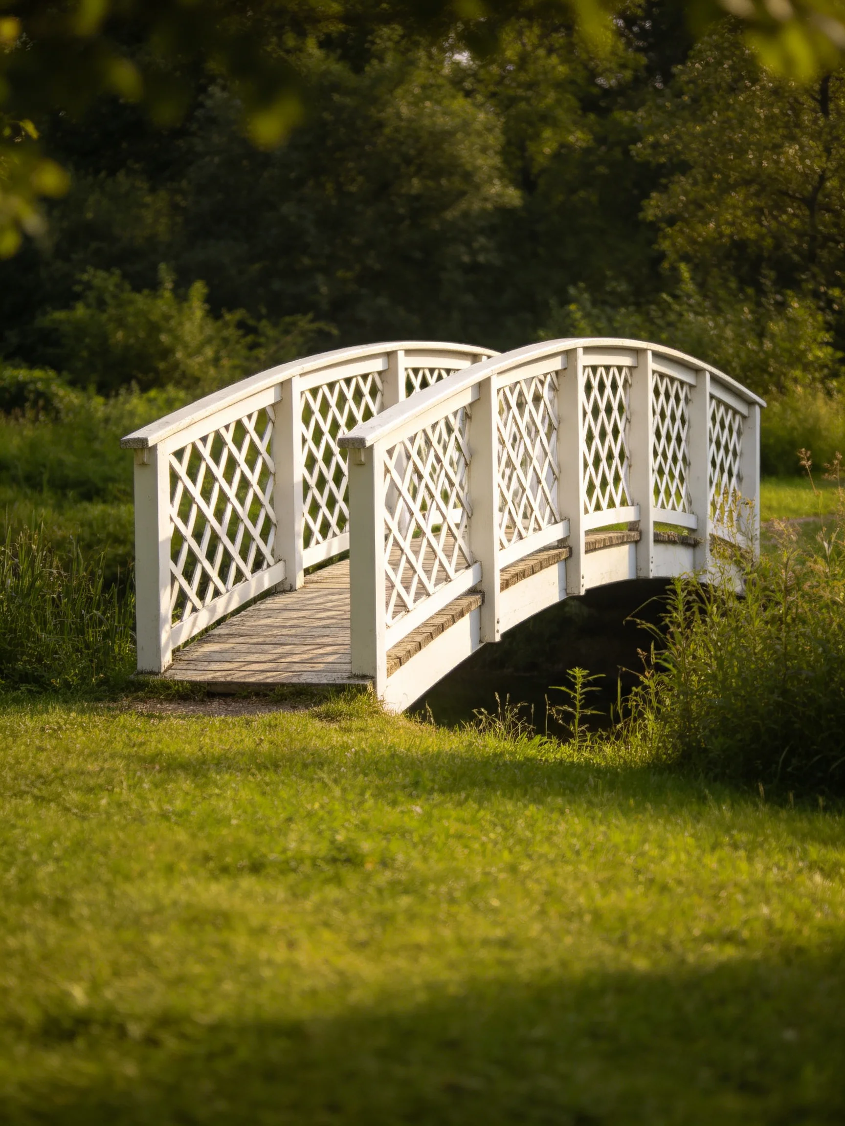 A white lattice bridge spans a small stream amid lush greenery