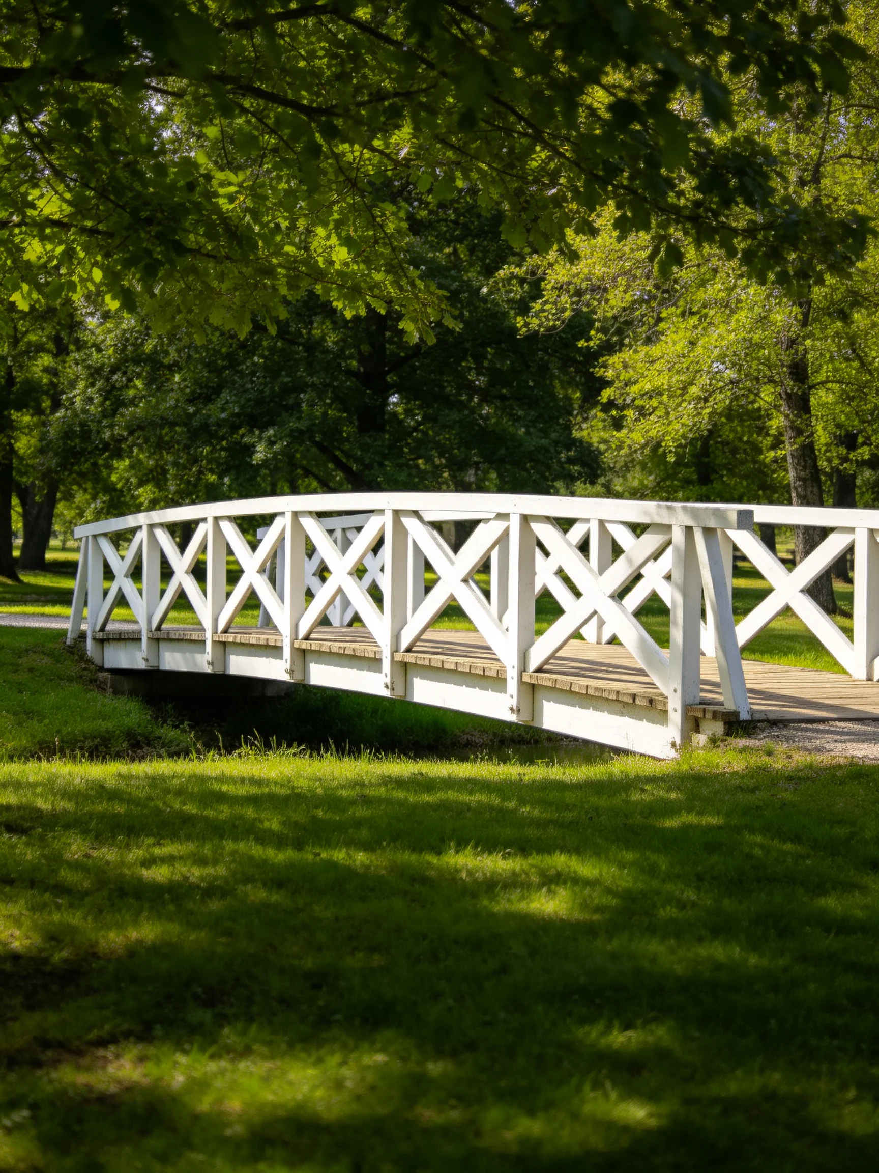 A white wooden bridge spans a small stream amid lush green trees