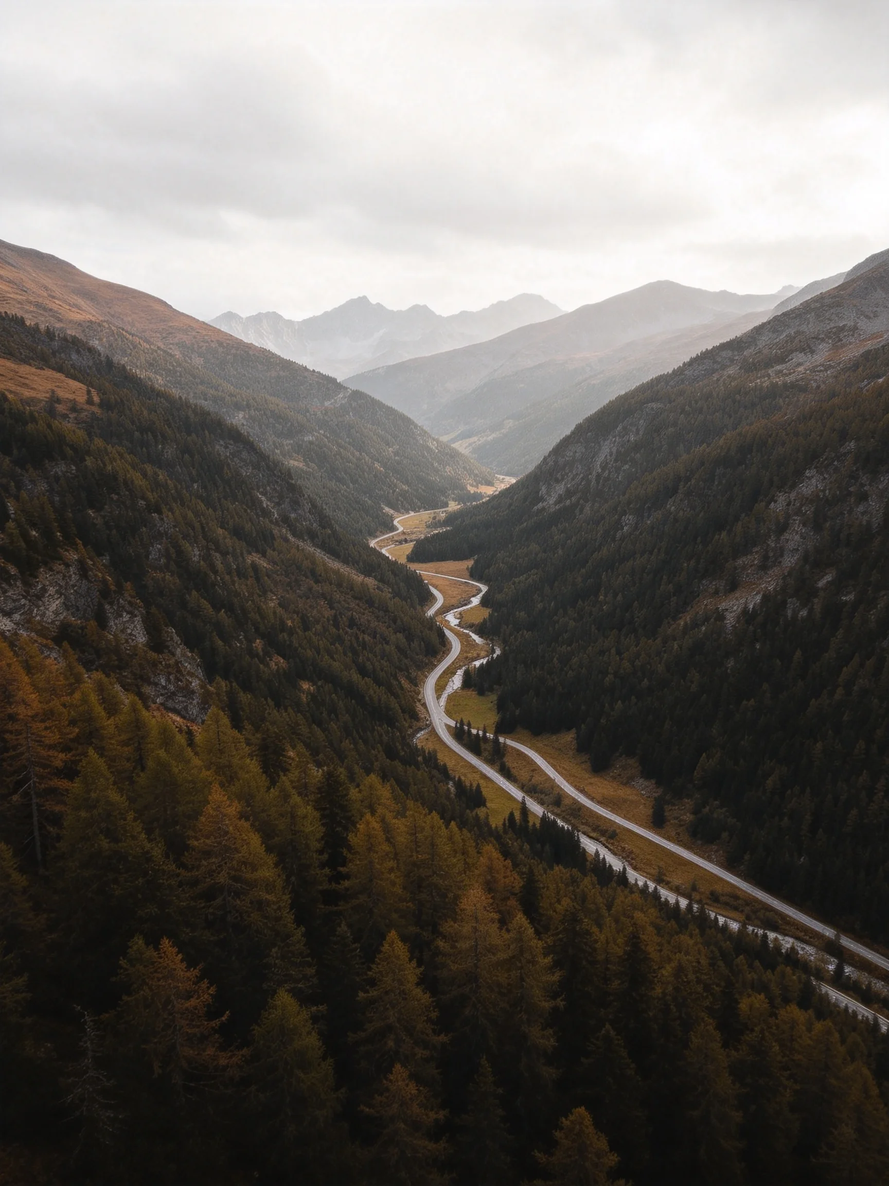A winding road cuts through an autumnal forested mountain valley