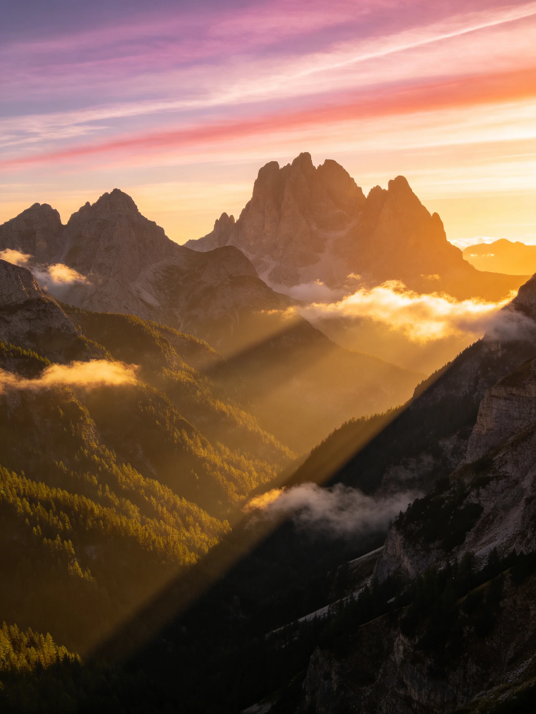 Dramatic mountain peaks at sunset with golden light beams and misty valleys