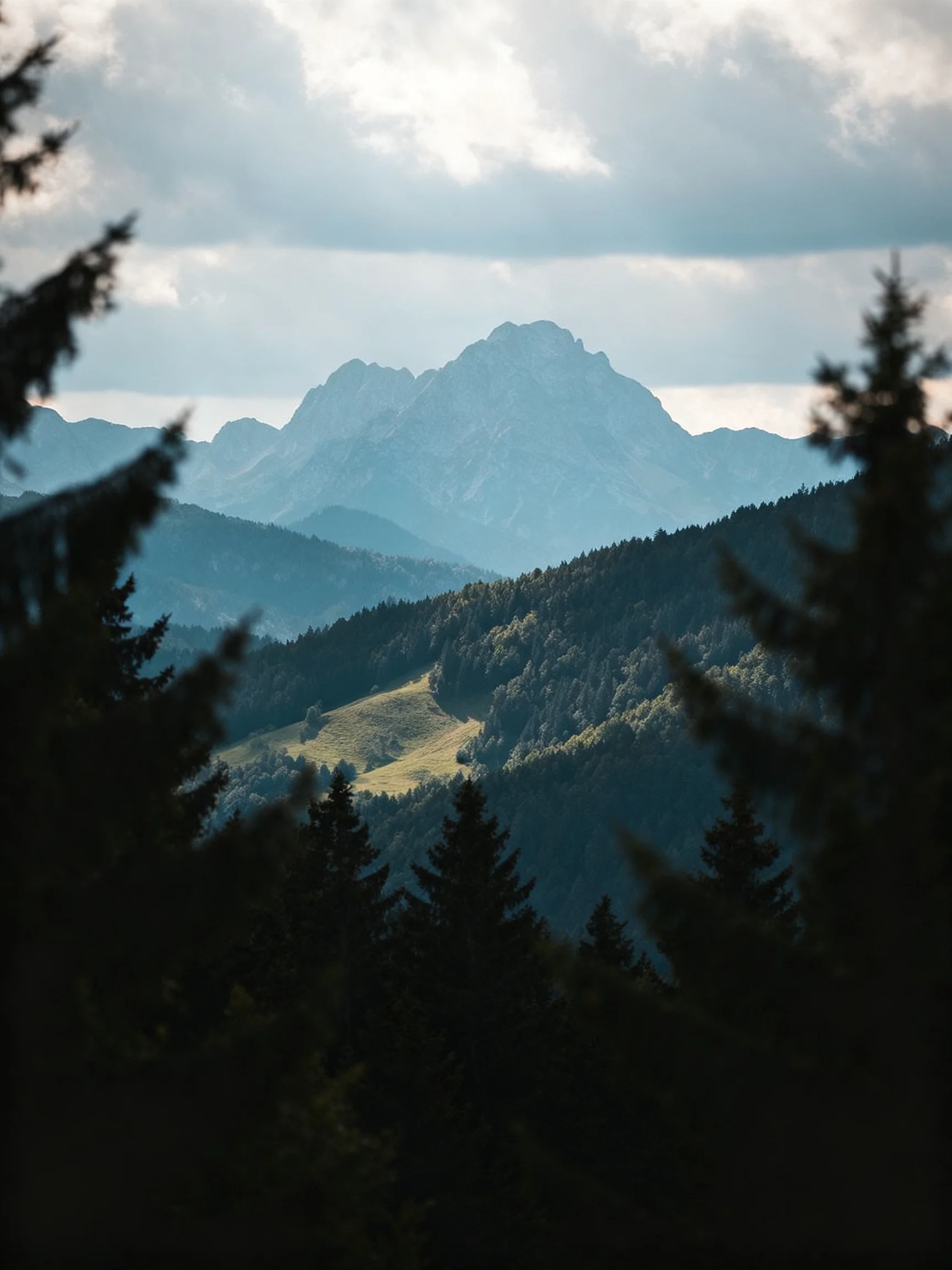 Majestic mountain peak rises above layered forested hills under cloudy sky