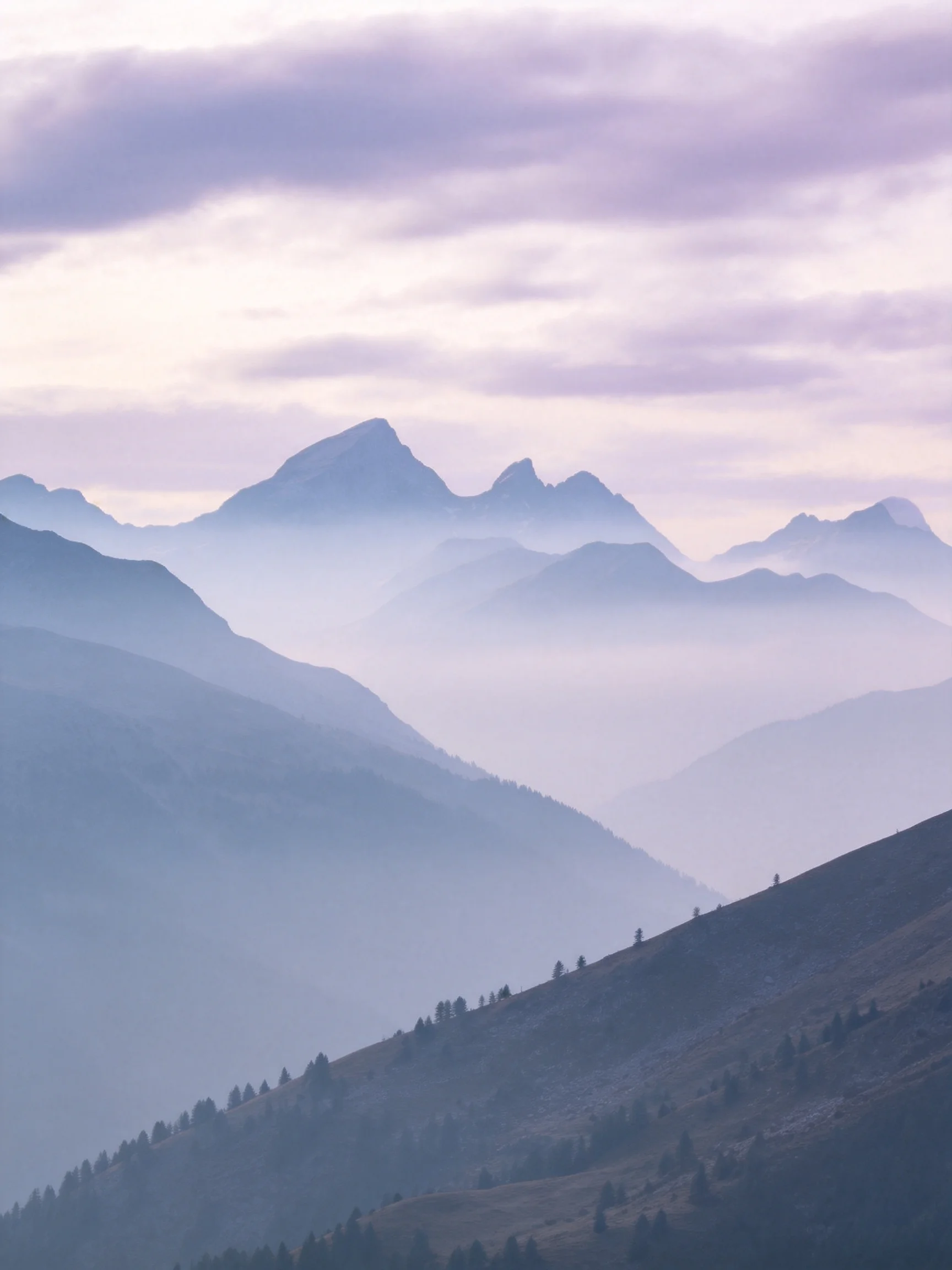 Misty mountain ranges with layered peaks under soft purple clouds
