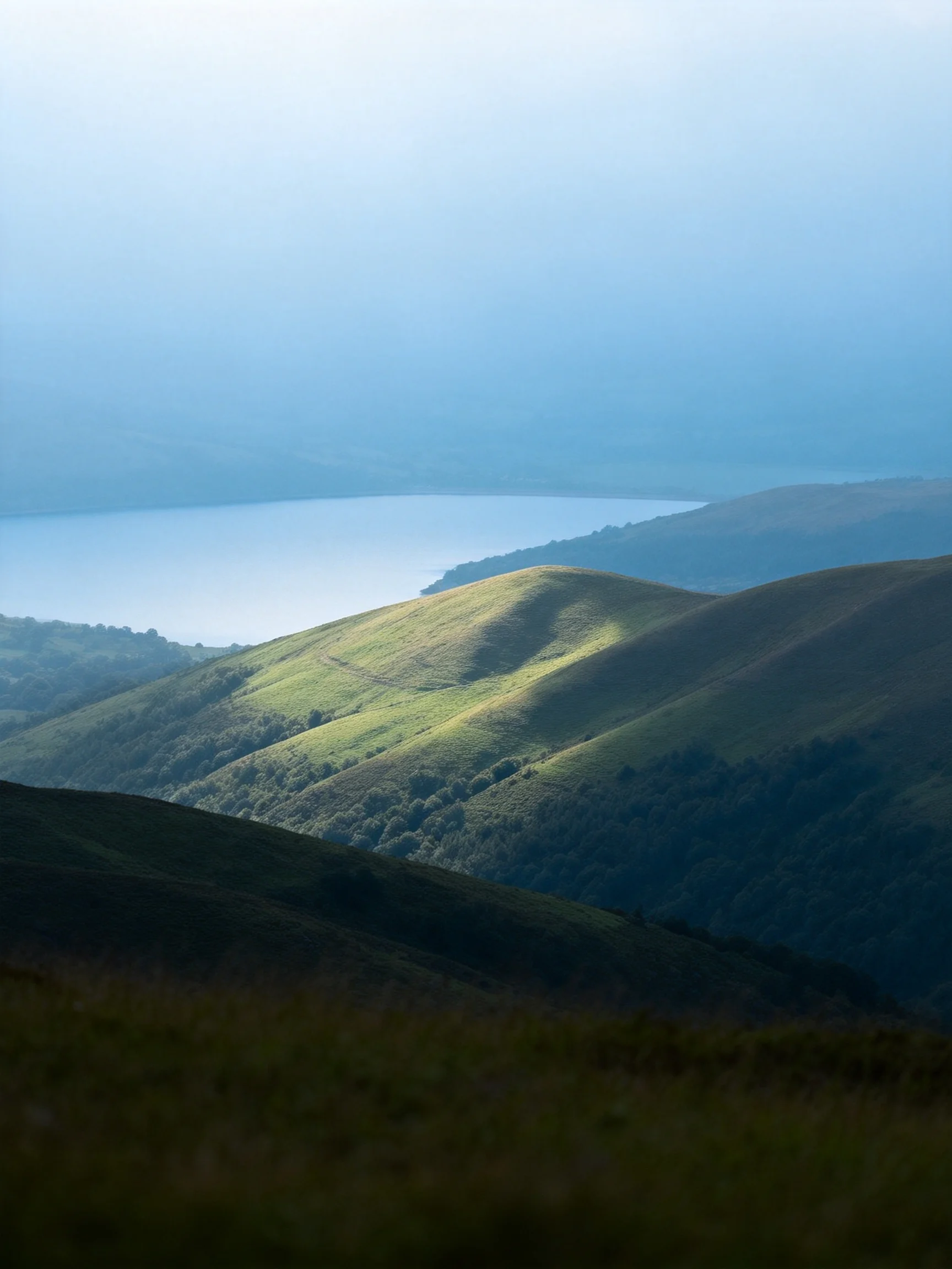 Rolling green hills with a serene blue lake in misty atmosphere