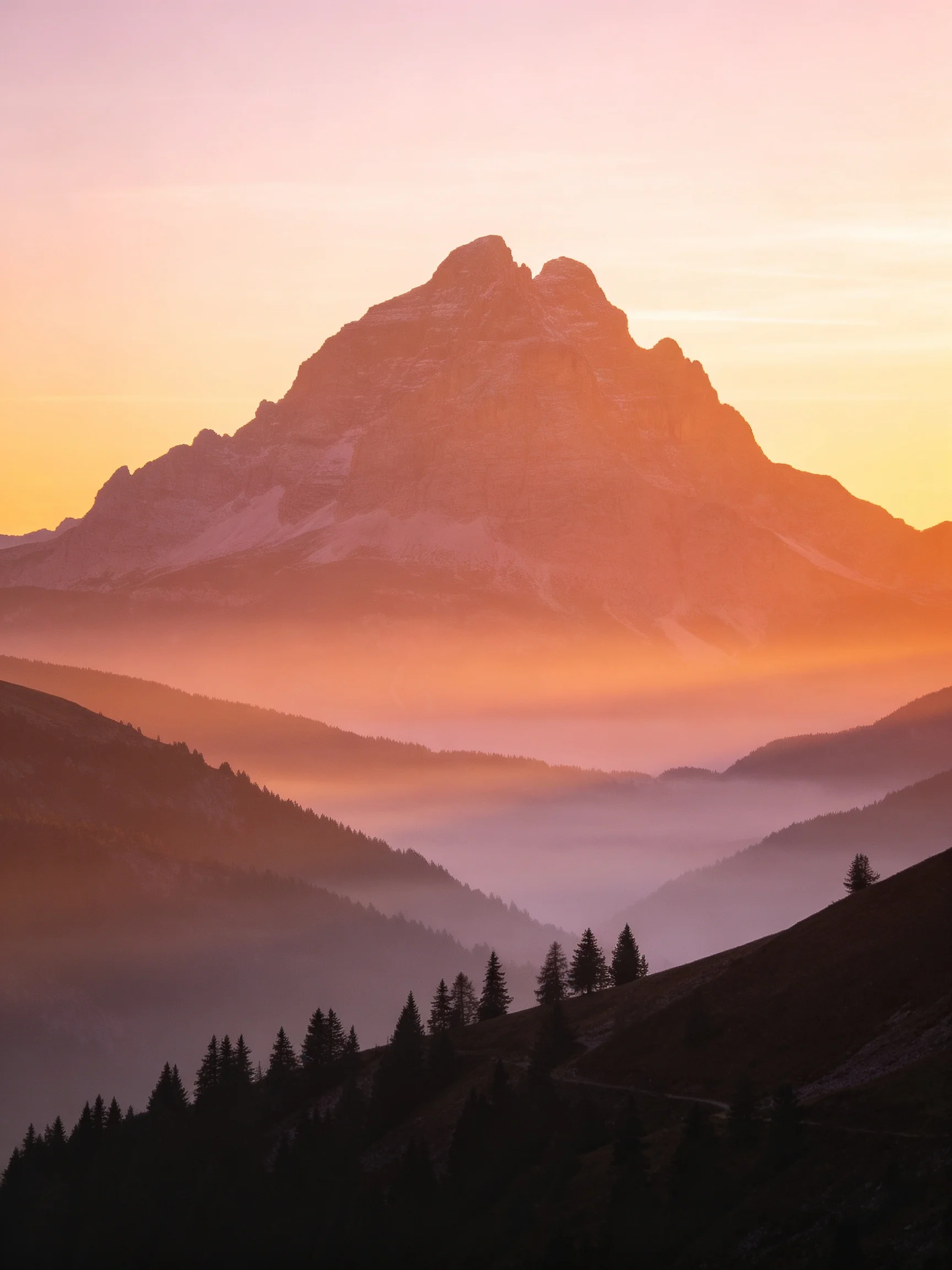 Silhouetted mountain peak amid layered valleys and hazy dawn light