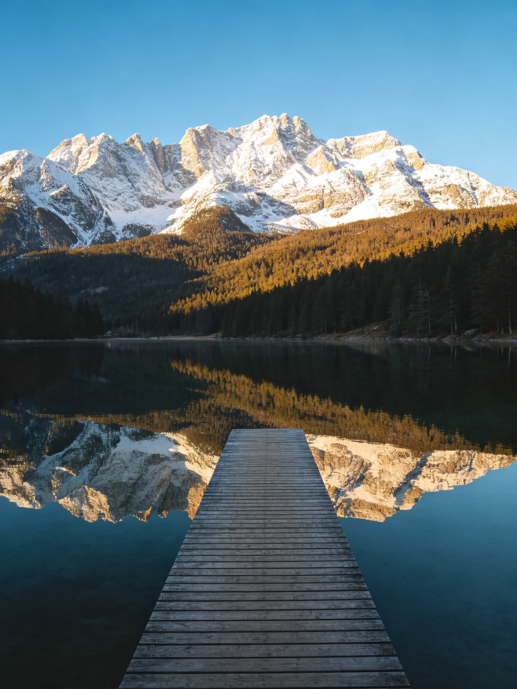 Snow - capped mountains reflected in a calm lake beside a wooden dock