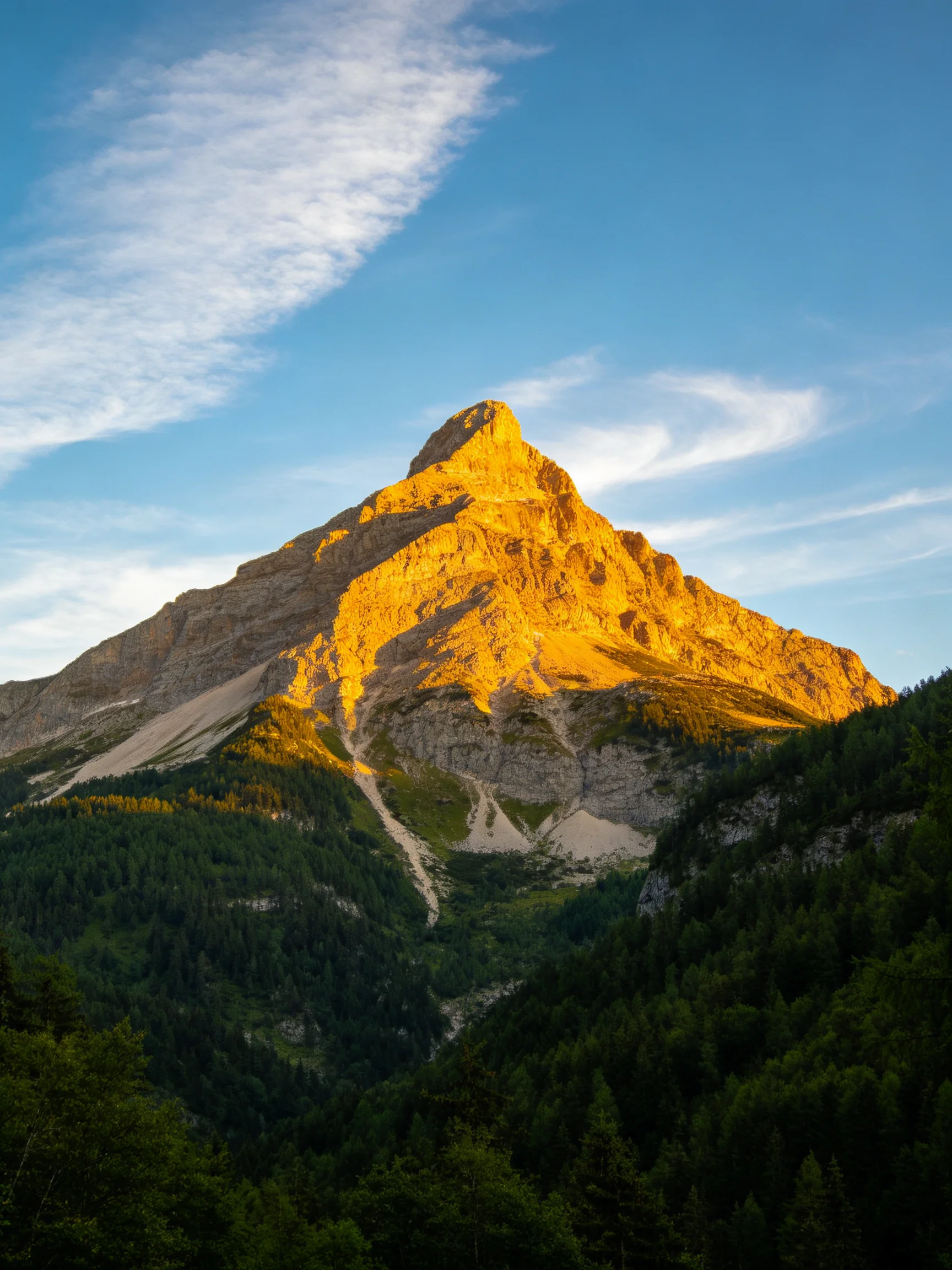 Sunlit golden mountain peak towers over dense green forests under clear blue sky