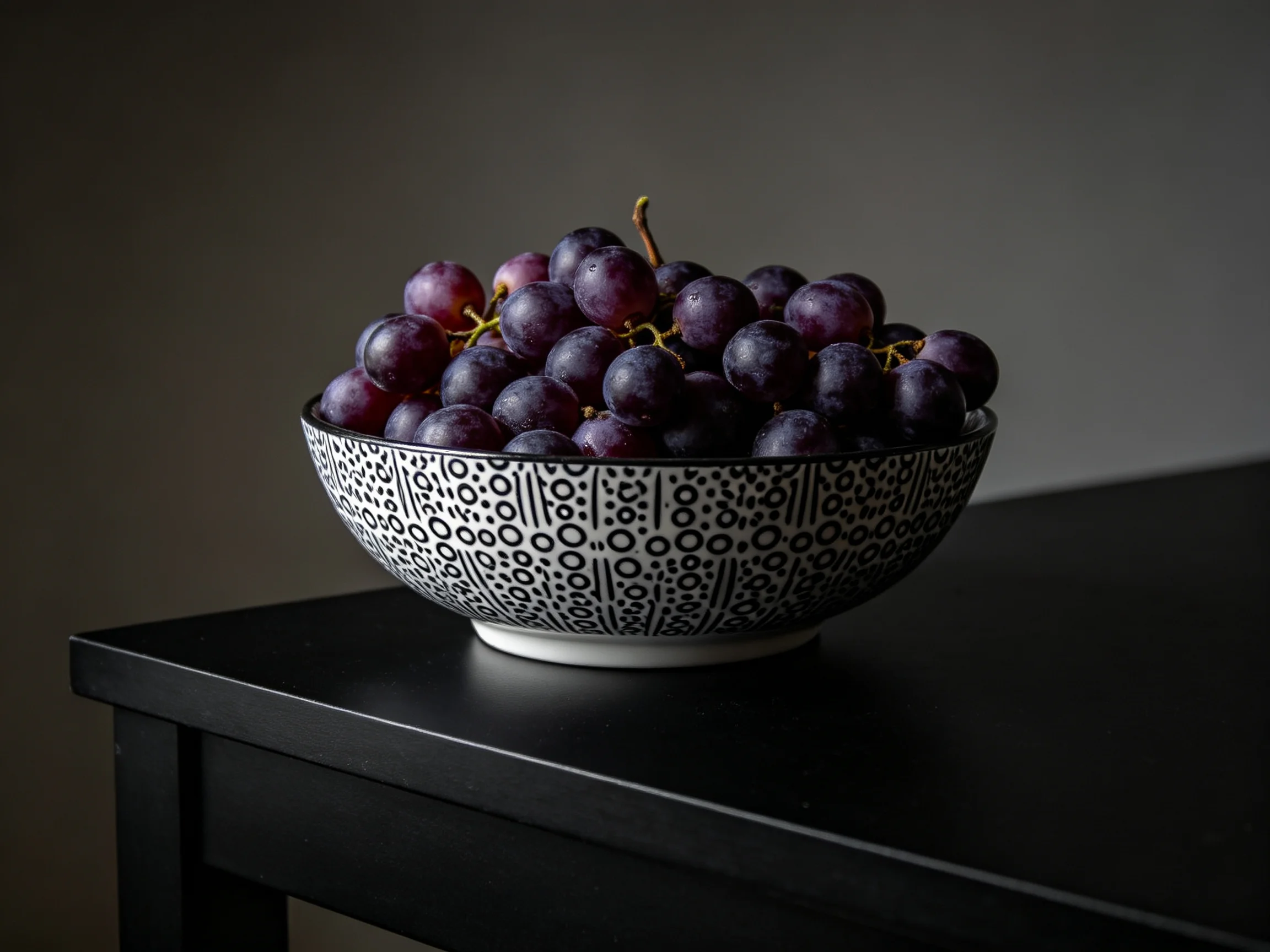 A black-and-white patterned bowl overflowing with dark purple grapes