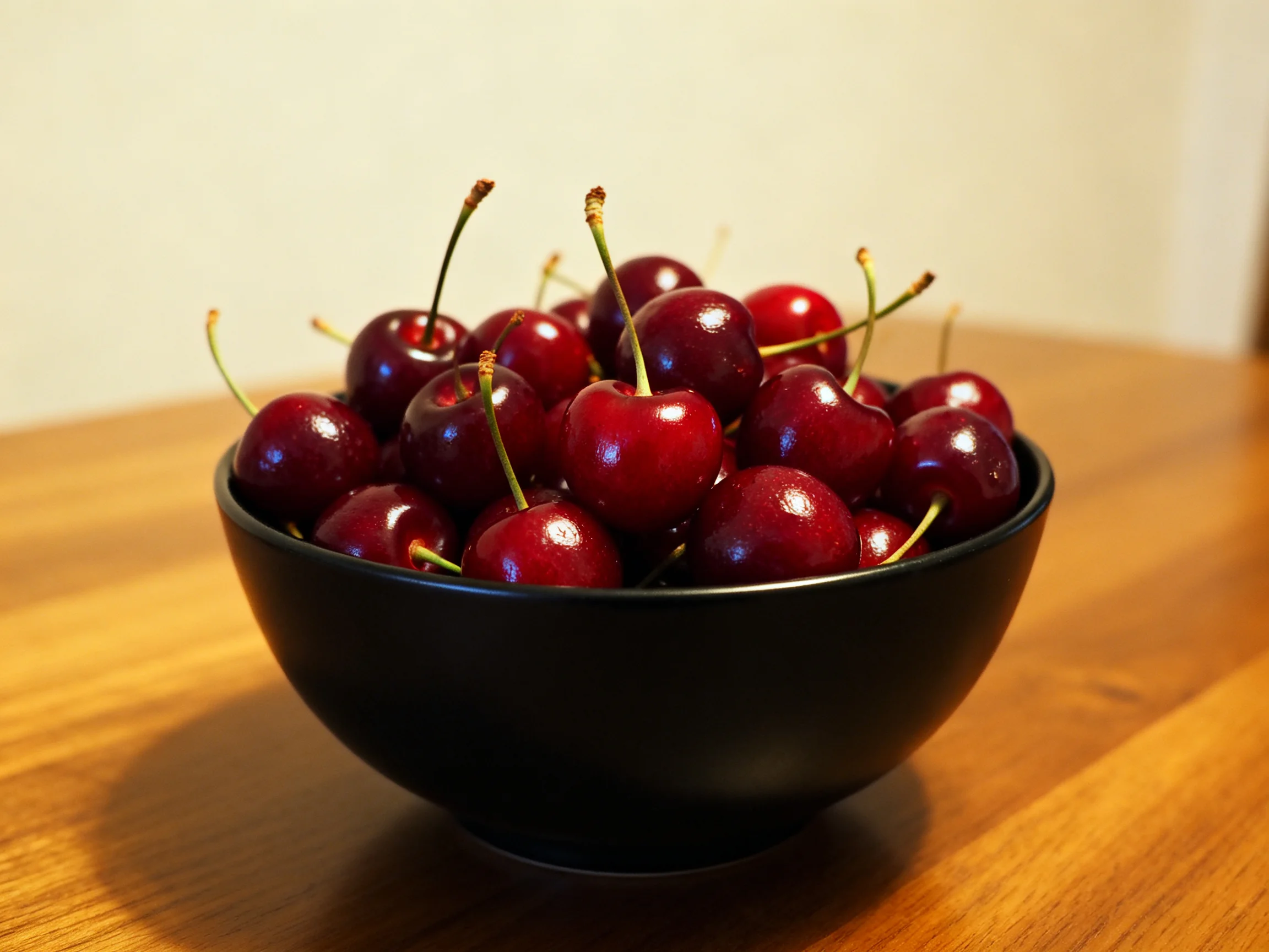 A black bowl brimming with glossy red cherries on a wooden table