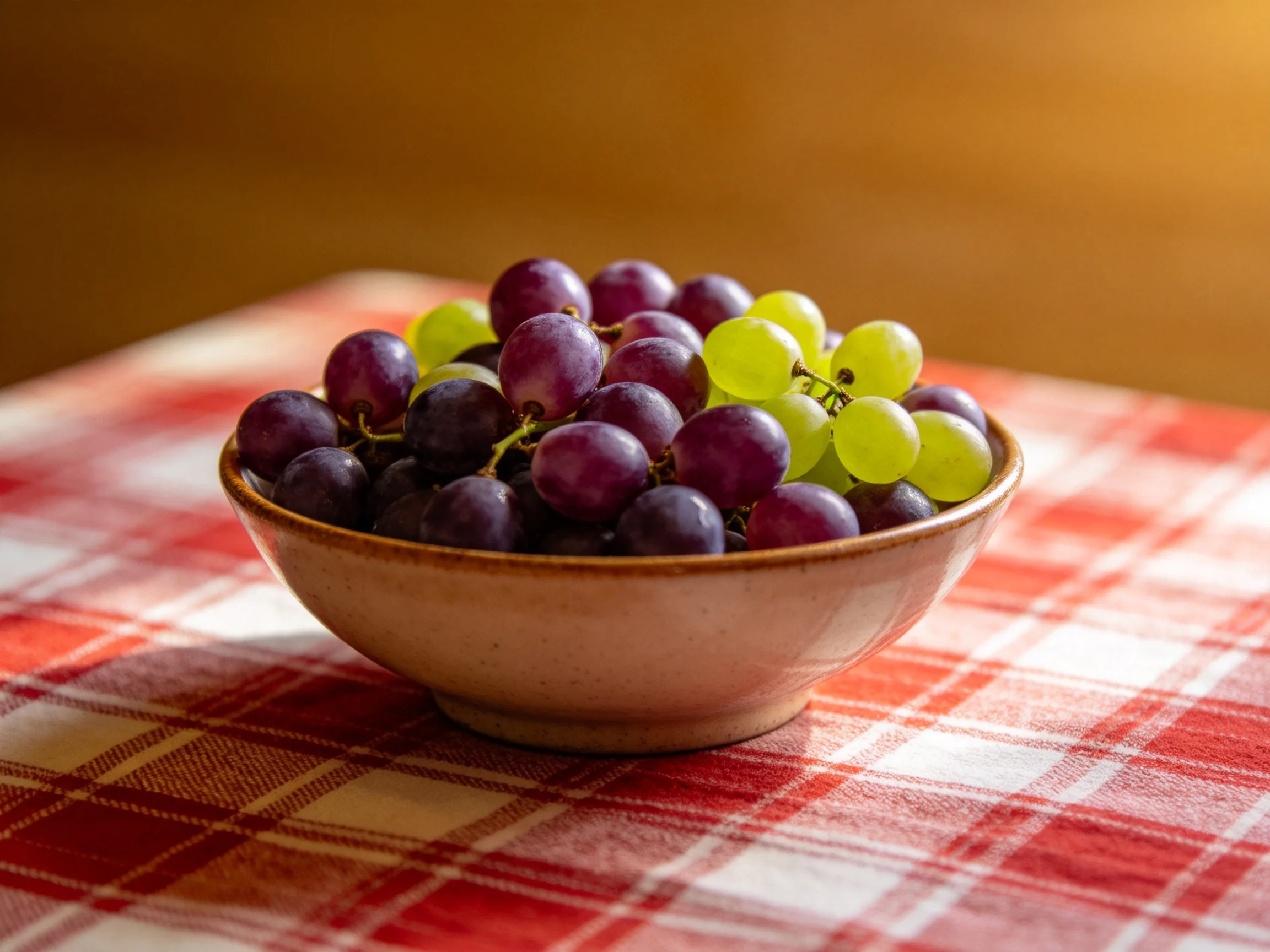 A bowl filled with purple and green grapes on a red plaid cloth