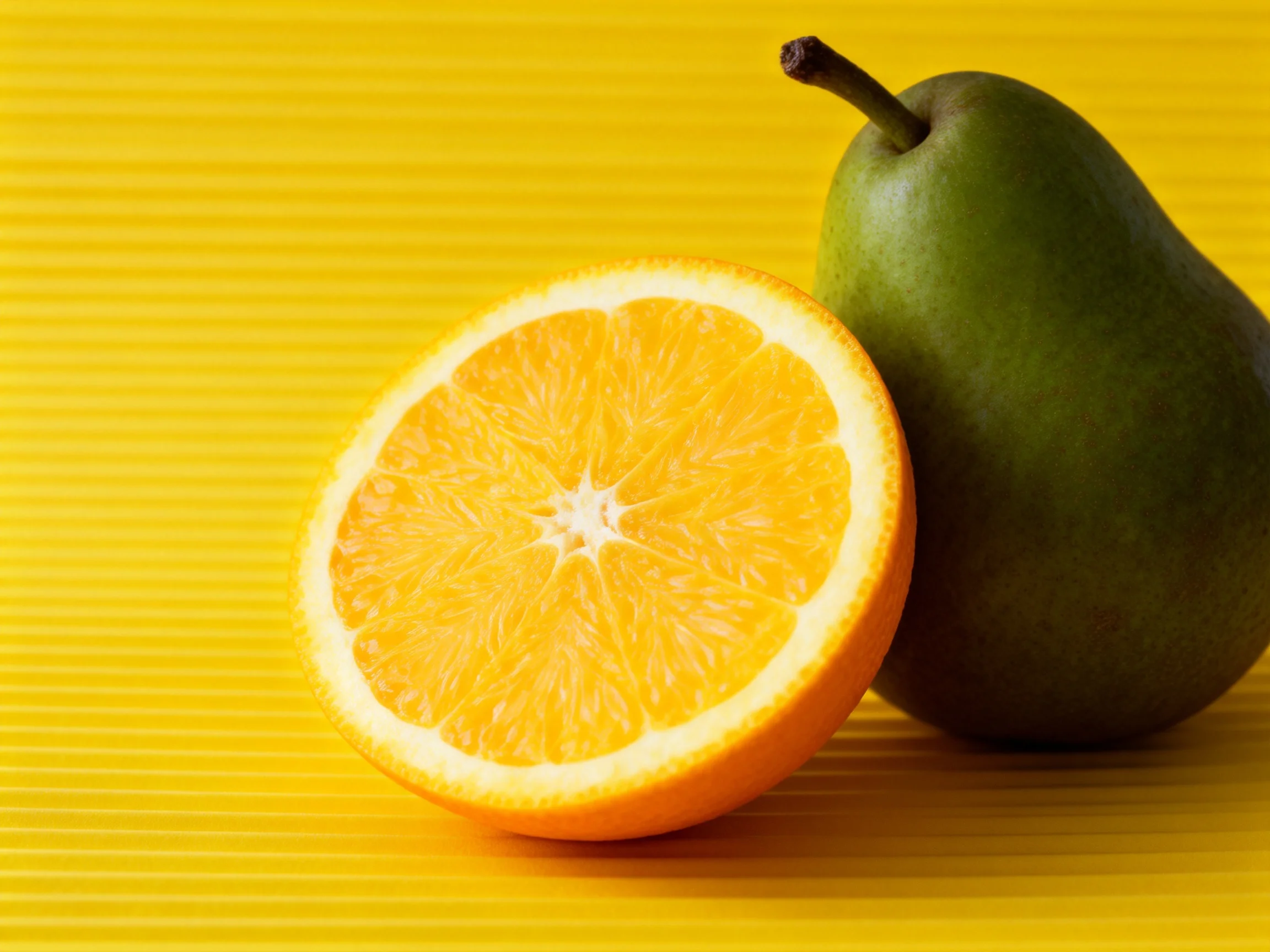 A bright orange half and a green pear sit on a yellow striped surface