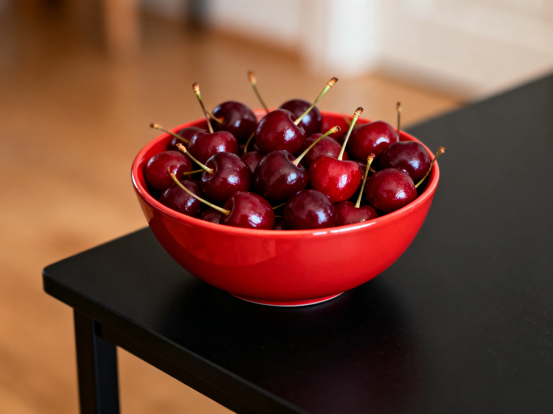 A bright red bowl brimming with glossy cherries sits on a sleek black table
