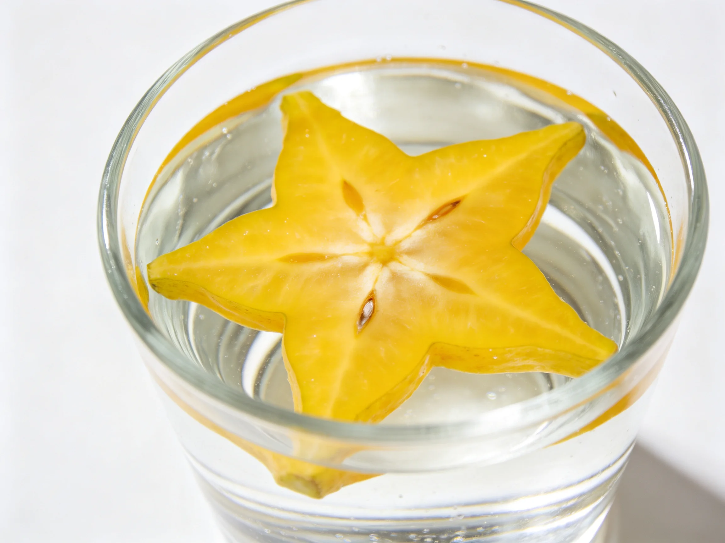 A bright yellow starfruit slice floating in a glass of clear water
