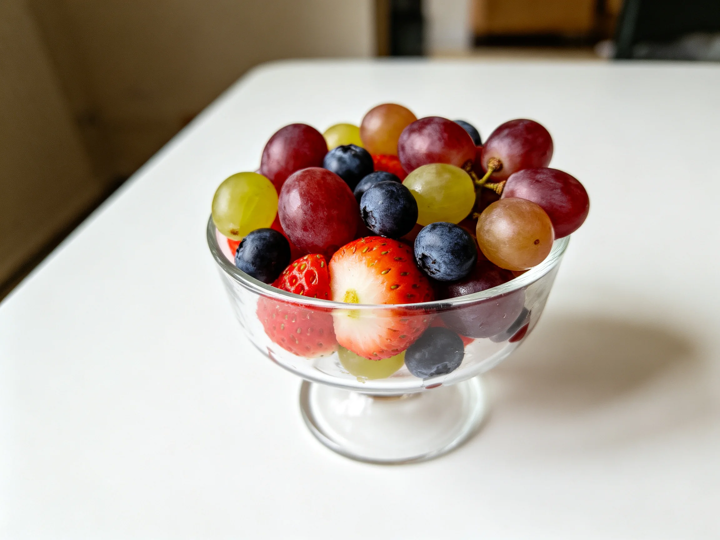 A clear glass bowl with assorted colorful fruits including strawberries, grapes, and blueberries