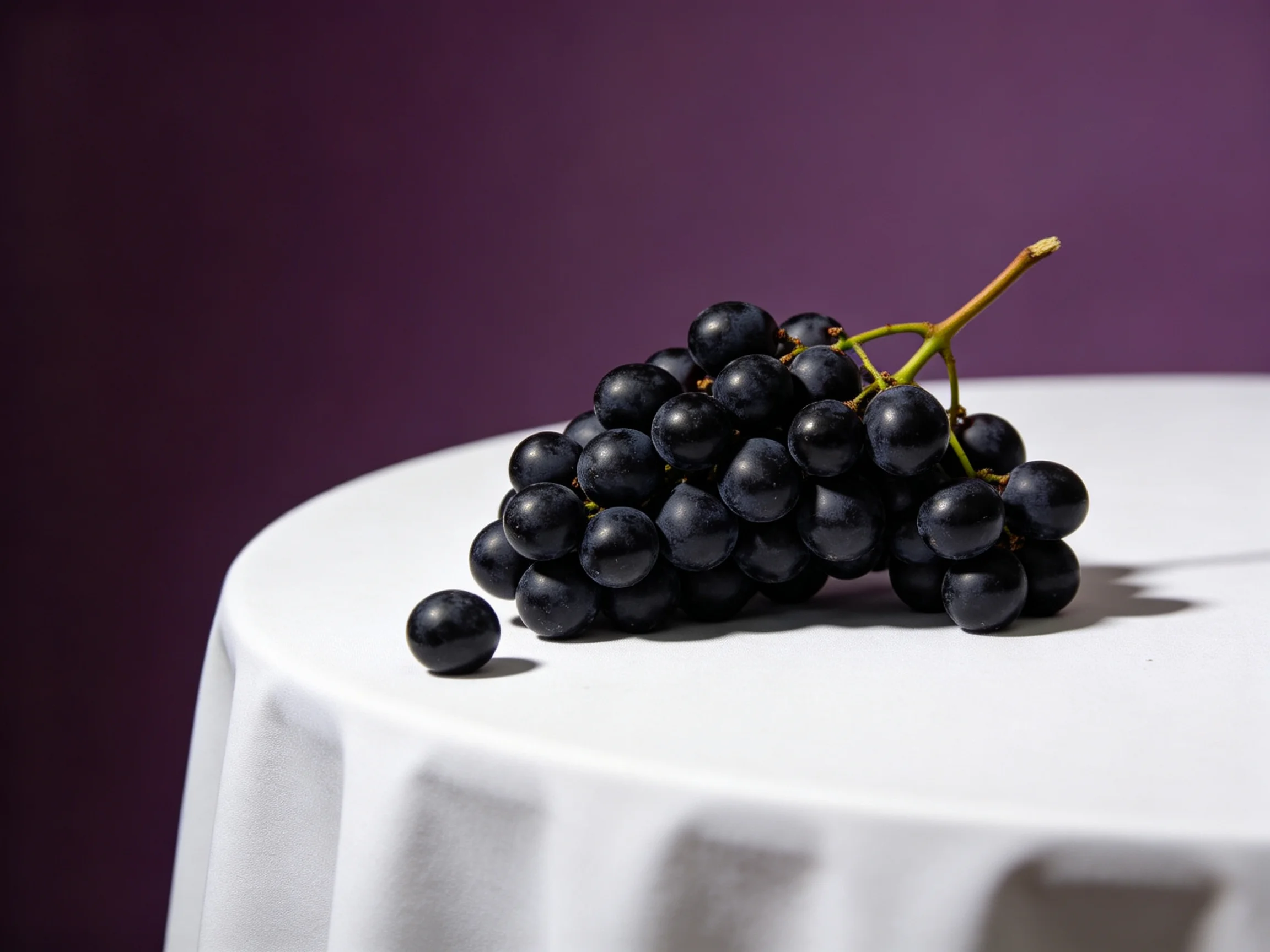 A cluster of dark purple grapes rests on a white tablecloth with a deep purple backdrop.