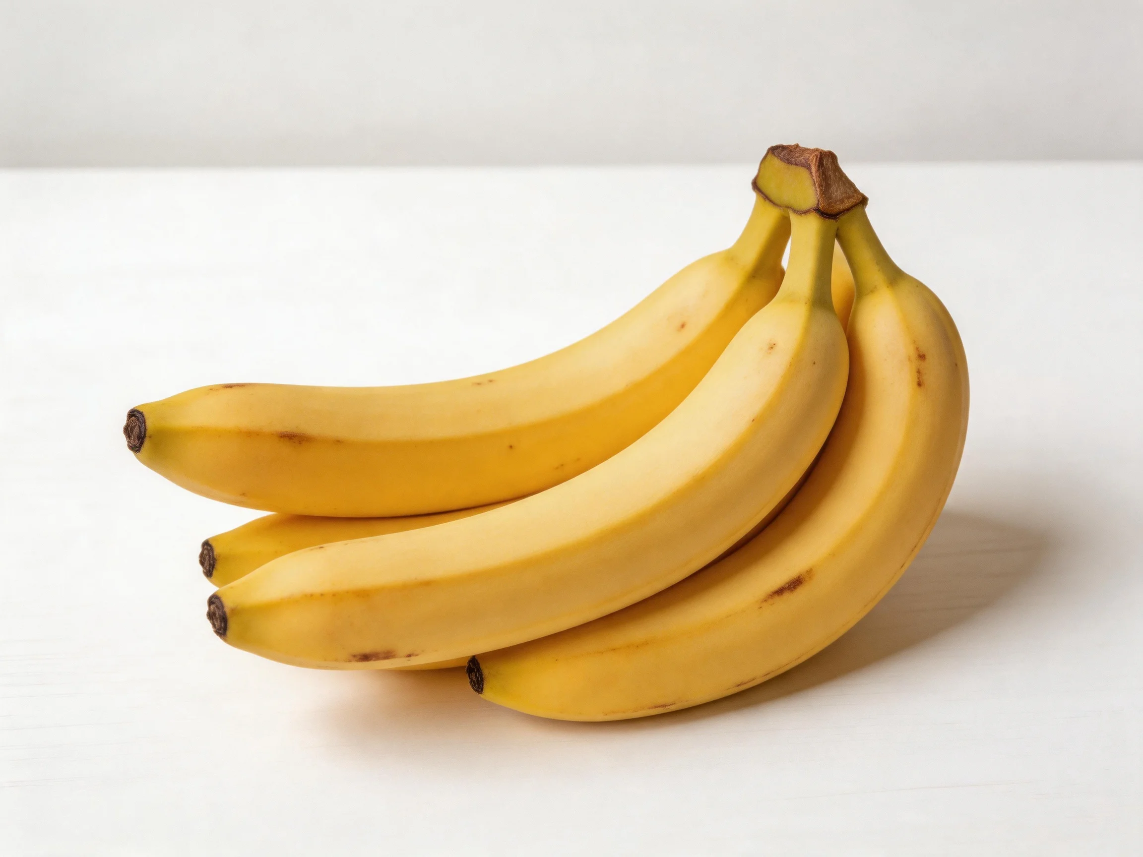 A cluster of four ripe yellow bananas on a white surface