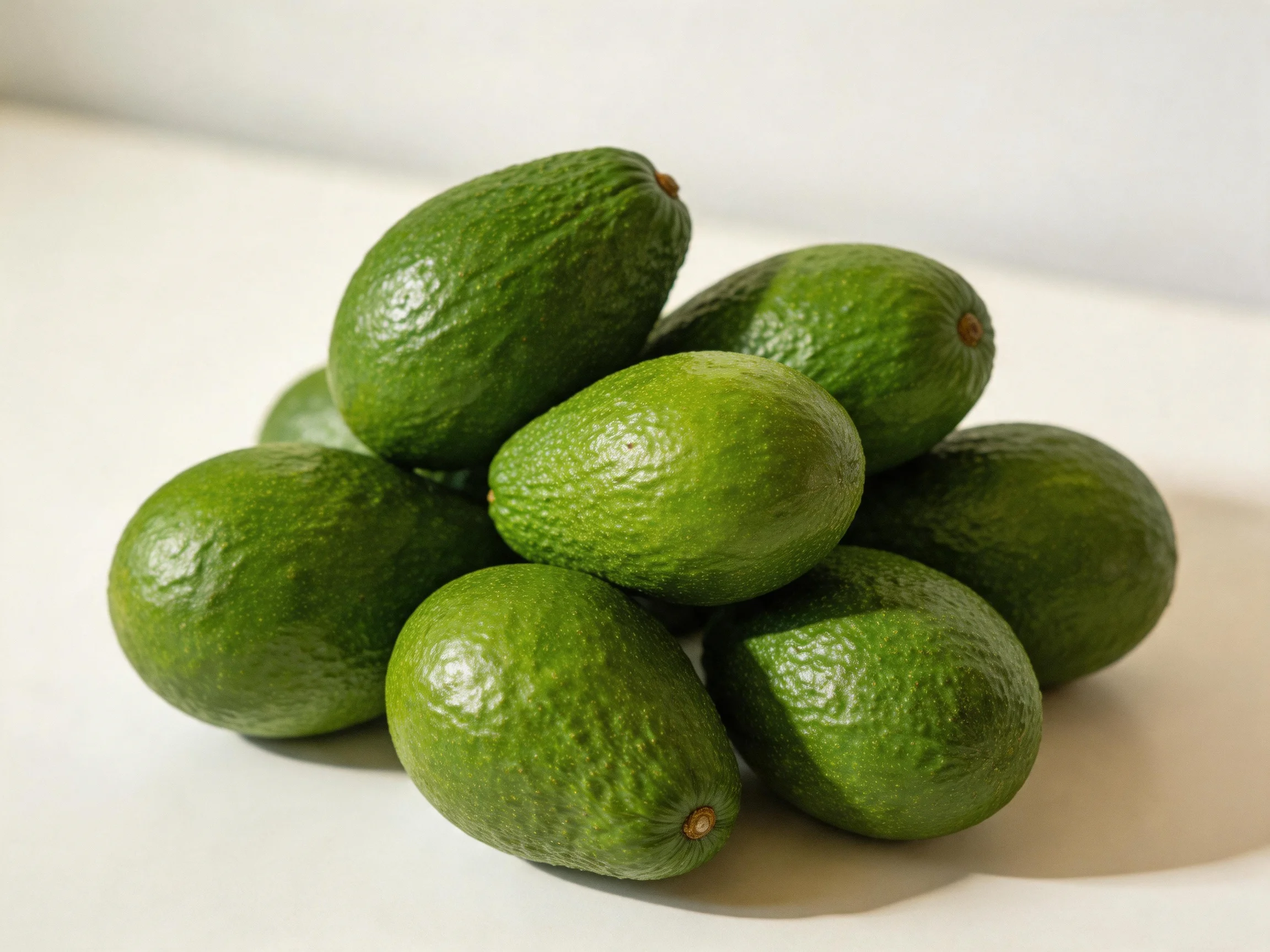 A cluster of fresh green avocados piled together on a white surface