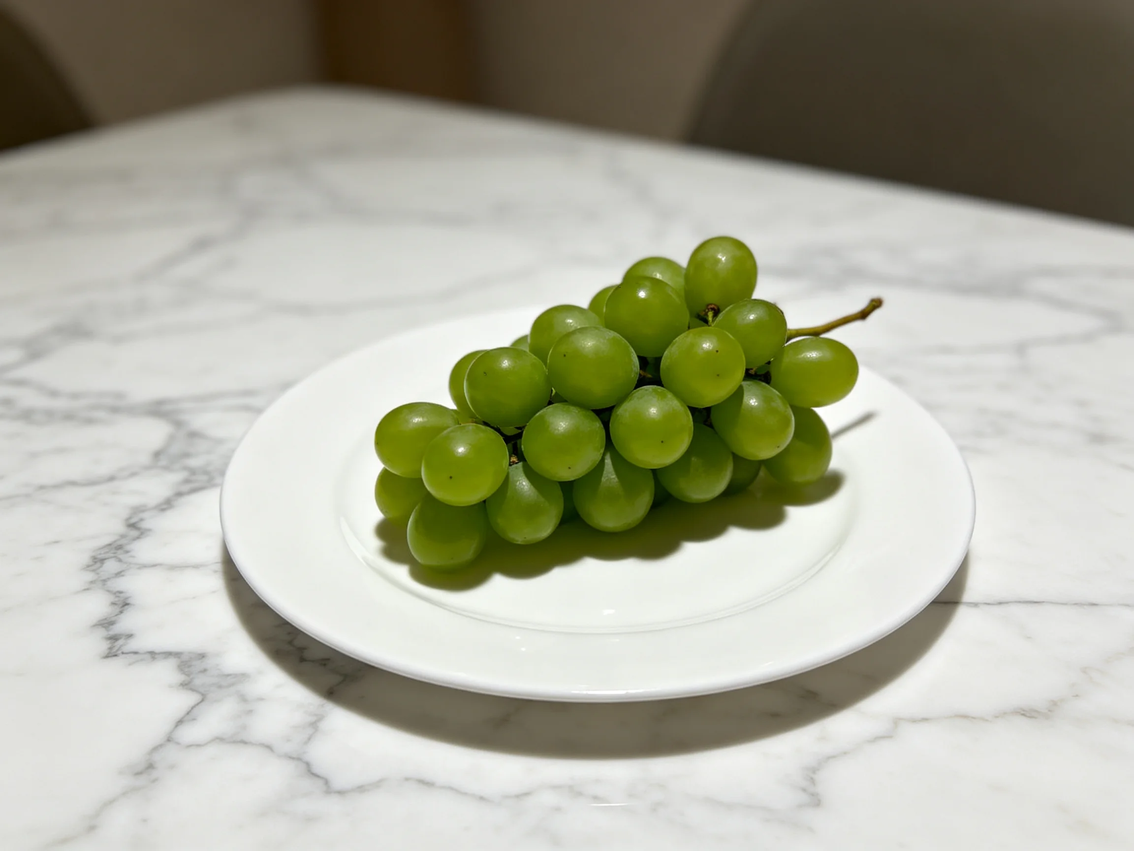 A cluster of fresh green grapes on a white plate atop a marble table