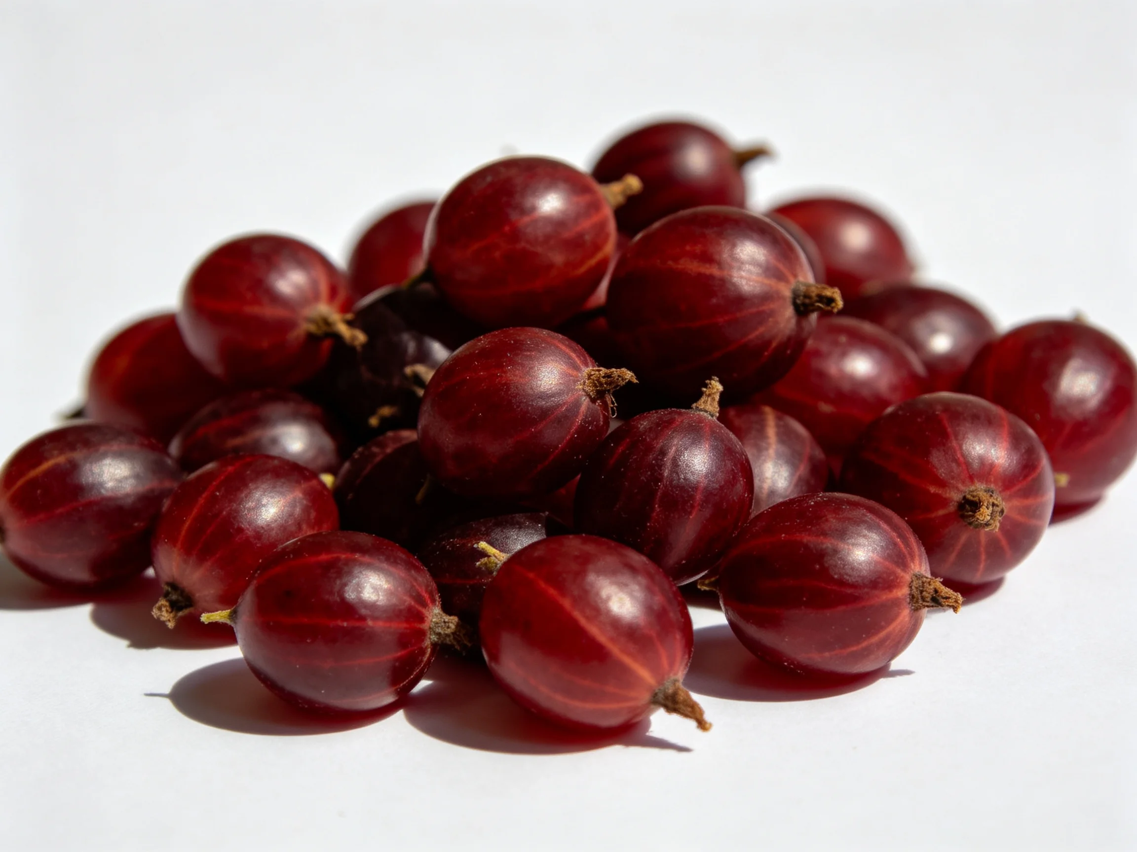 A cluster of glossy dark red gooseberries on a plain white backdrop