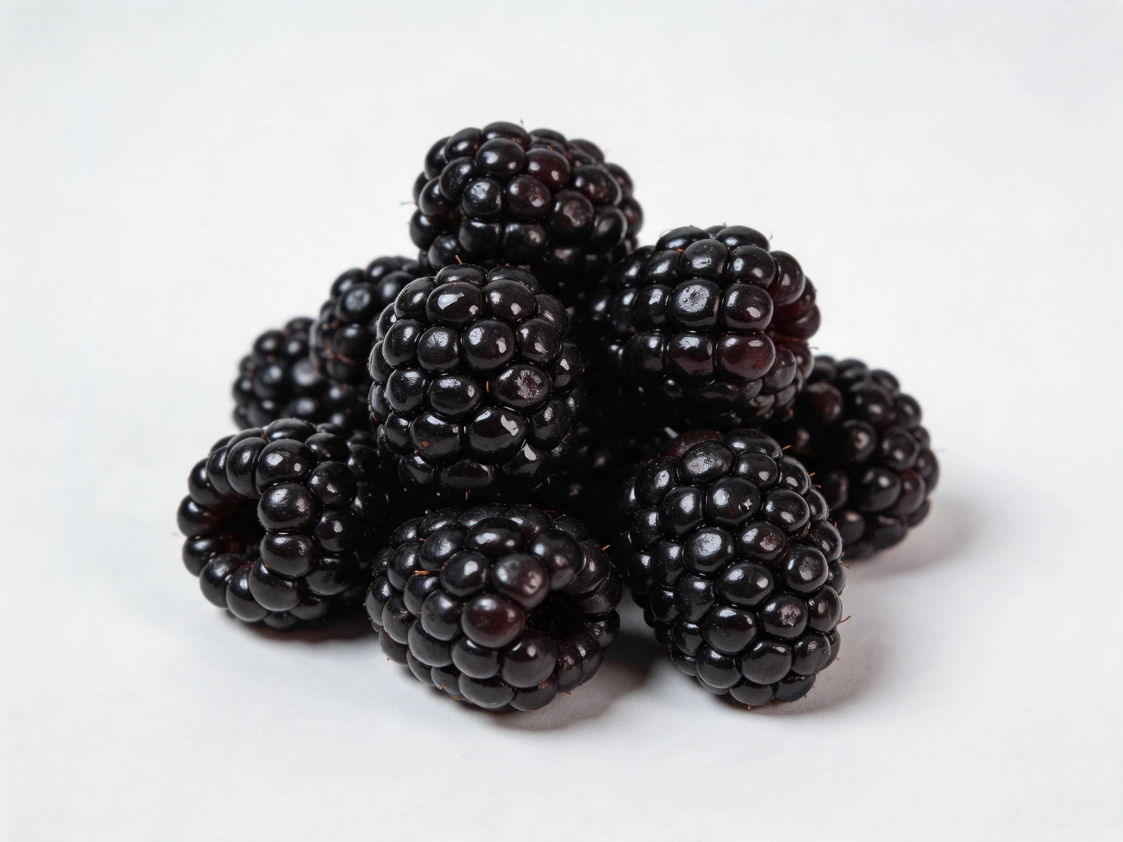 A cluster of glossy, deep-purple blackberries piled on a plain white surface