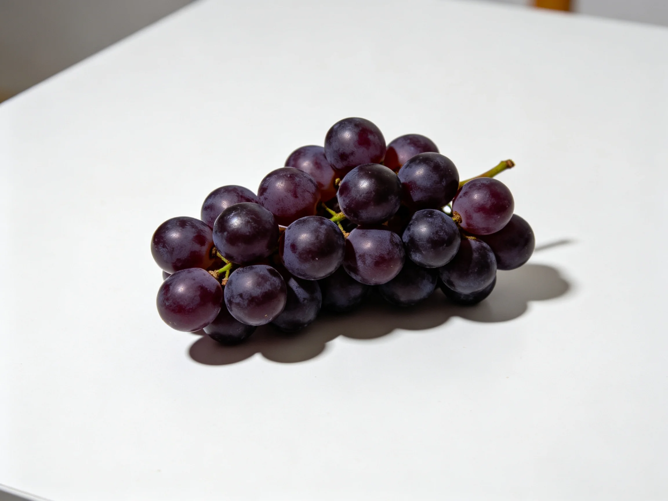 A cluster of plump dark purple grapes rests on a bright white surface