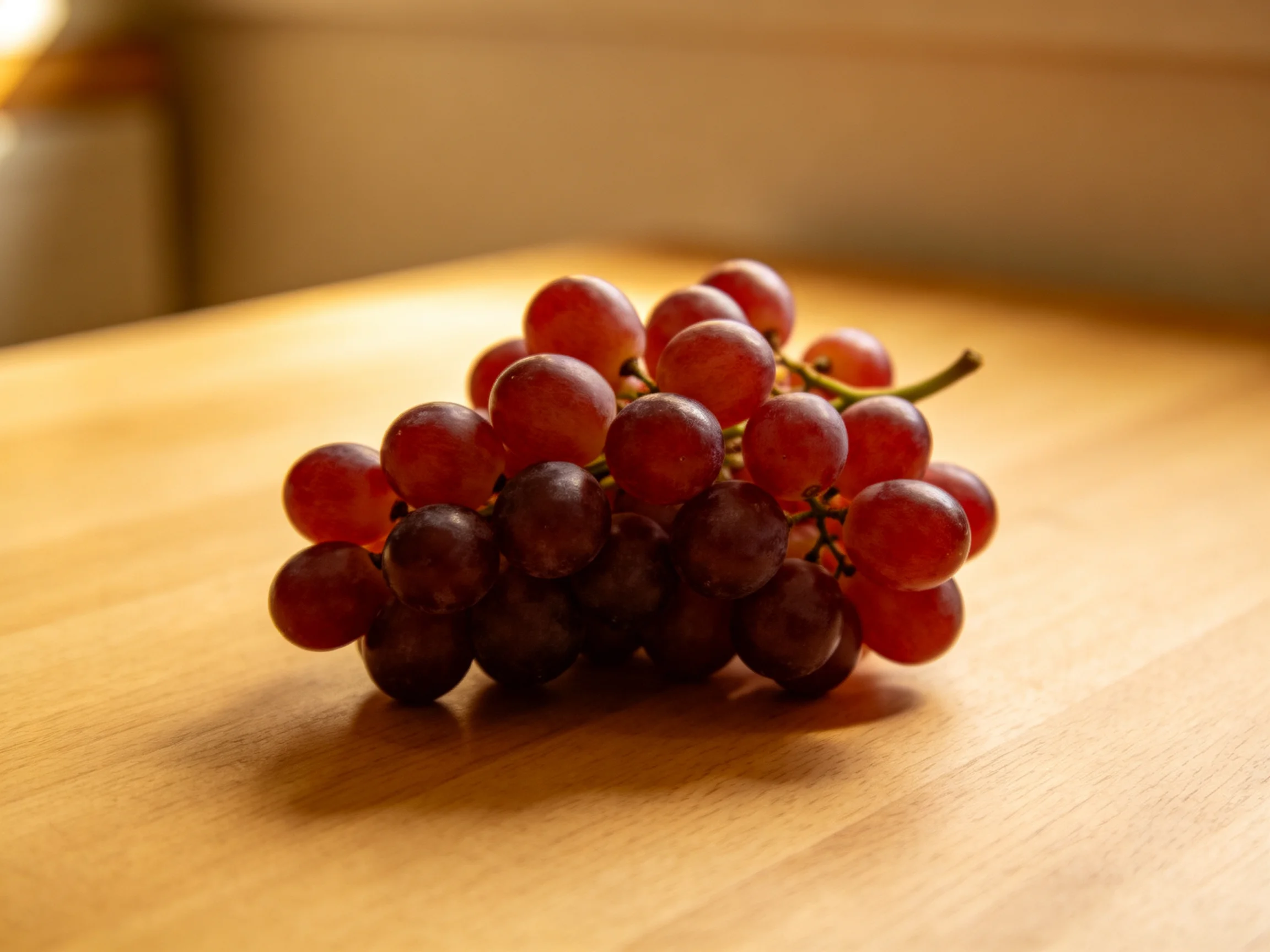 A cluster of red and dark purple grapes rests on a wooden surface.