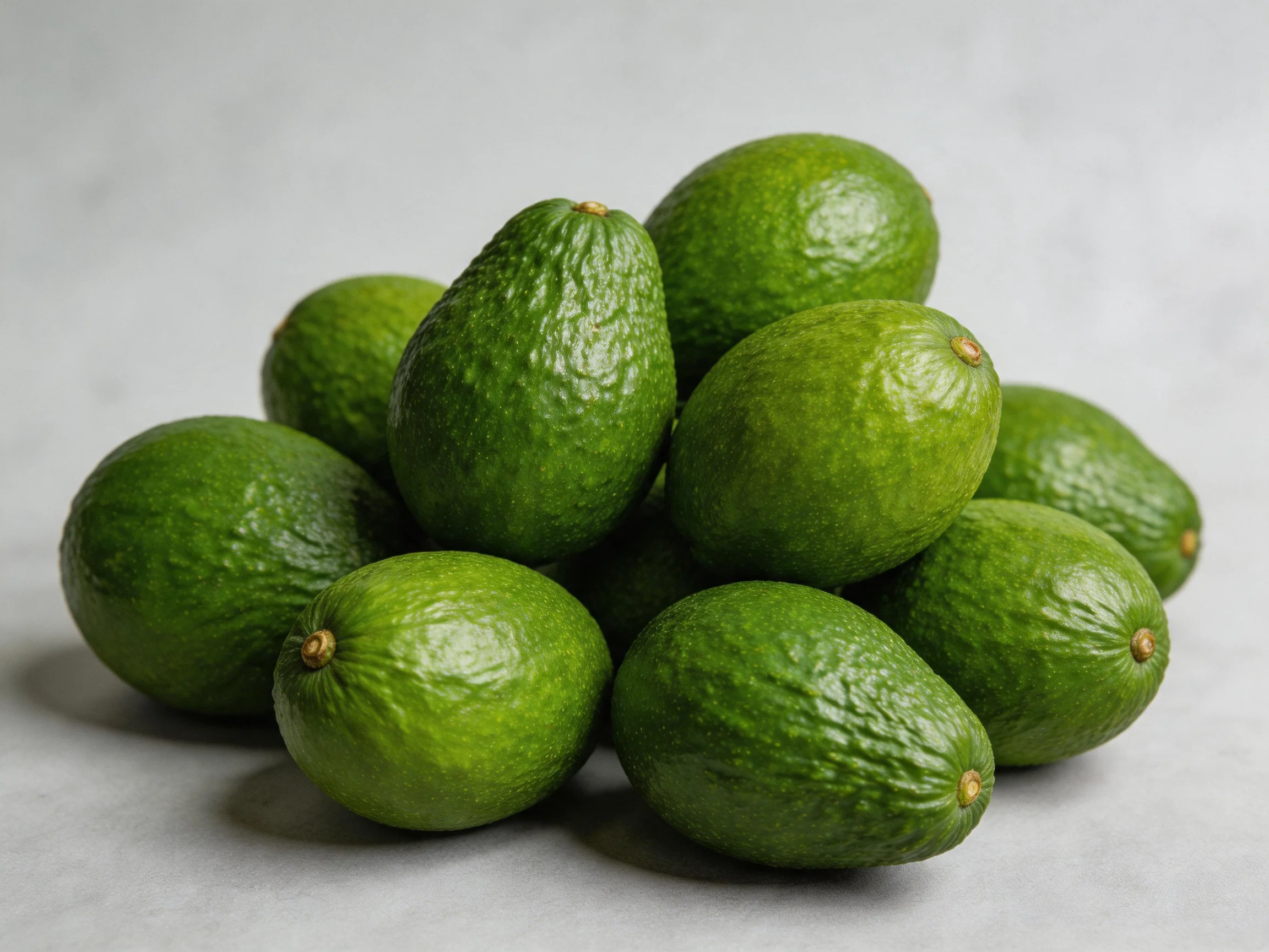 A cluster of vibrant green avocados piled closely on a neutral surface