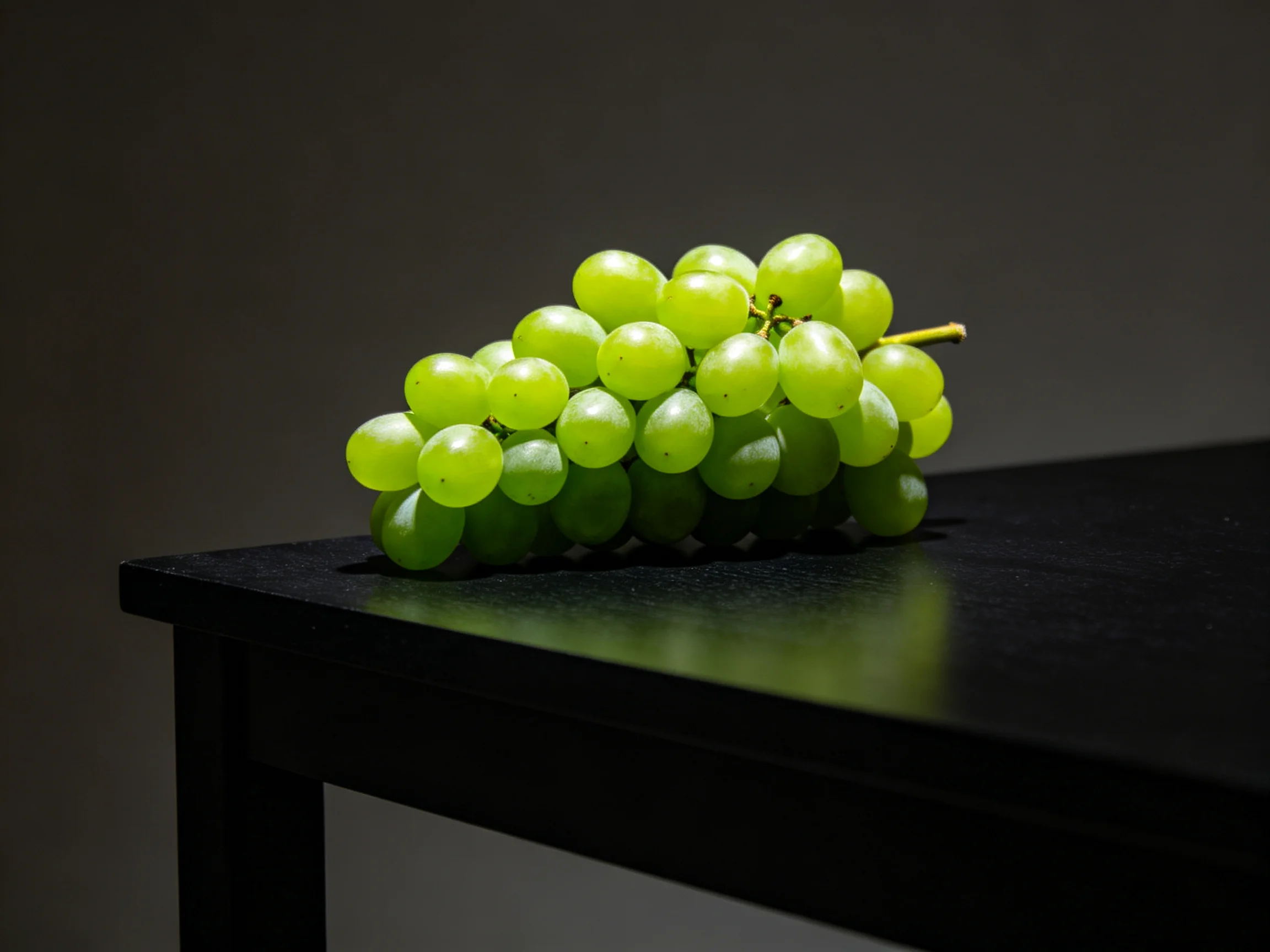 A cluster of vibrant green grapes rests on a sleek black surface