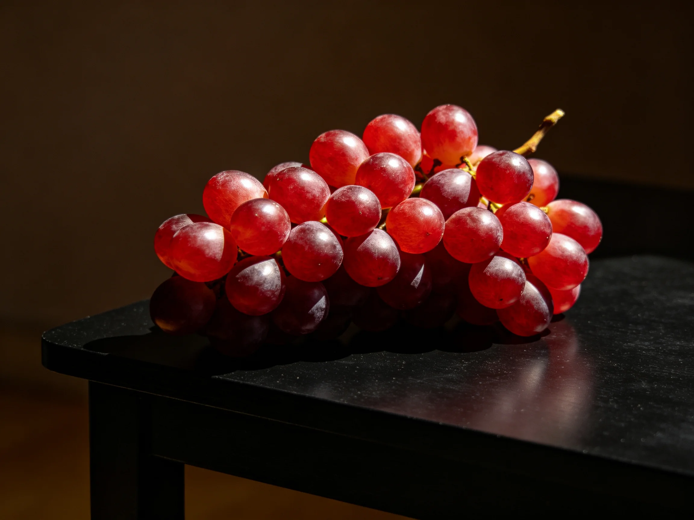 A cluster of vibrant red grapes rests on a glossy black surface