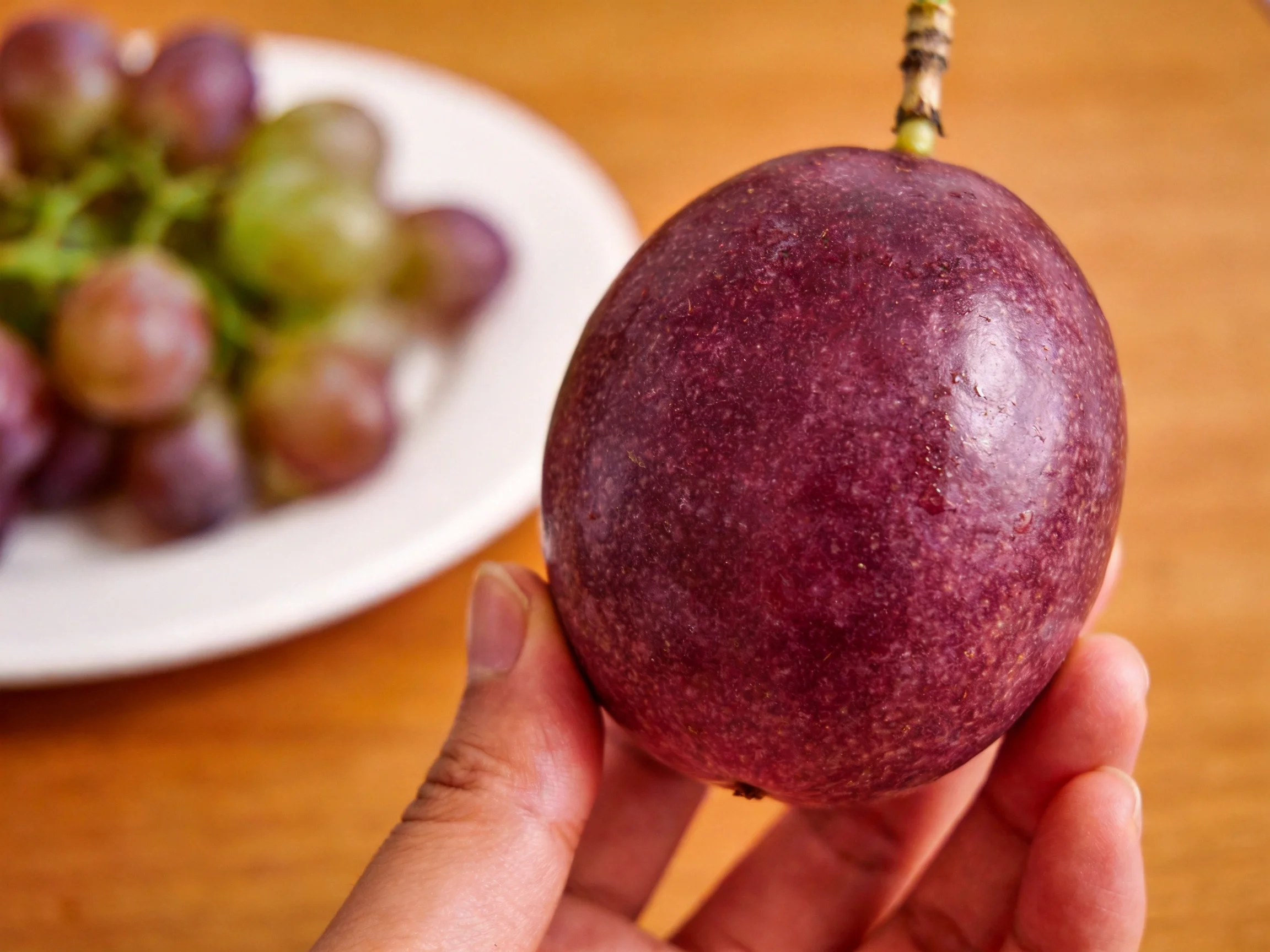 A deep purple passion fruit held near colorful grapes
