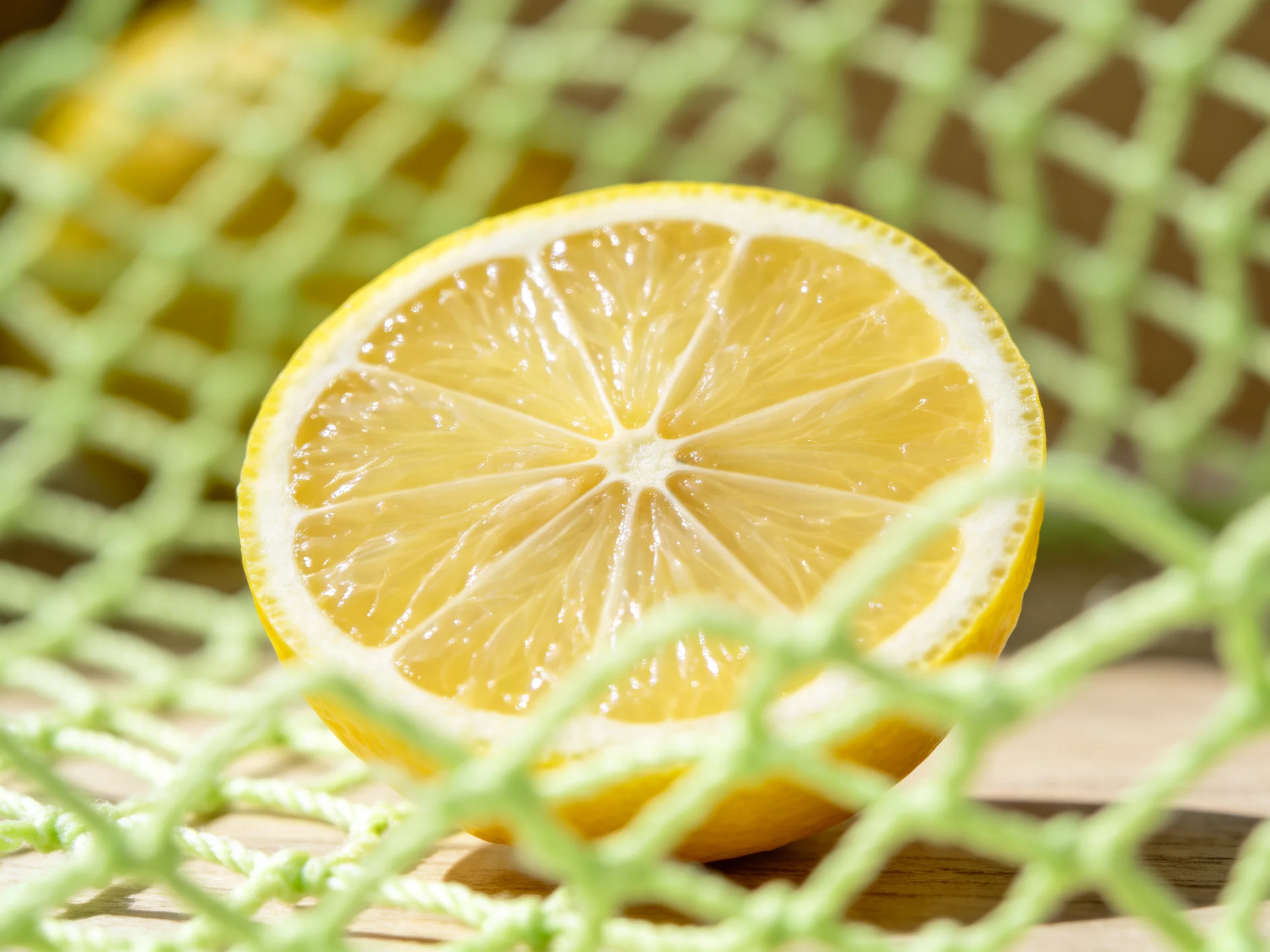 A fresh lemon half with juicy segments behind green netting