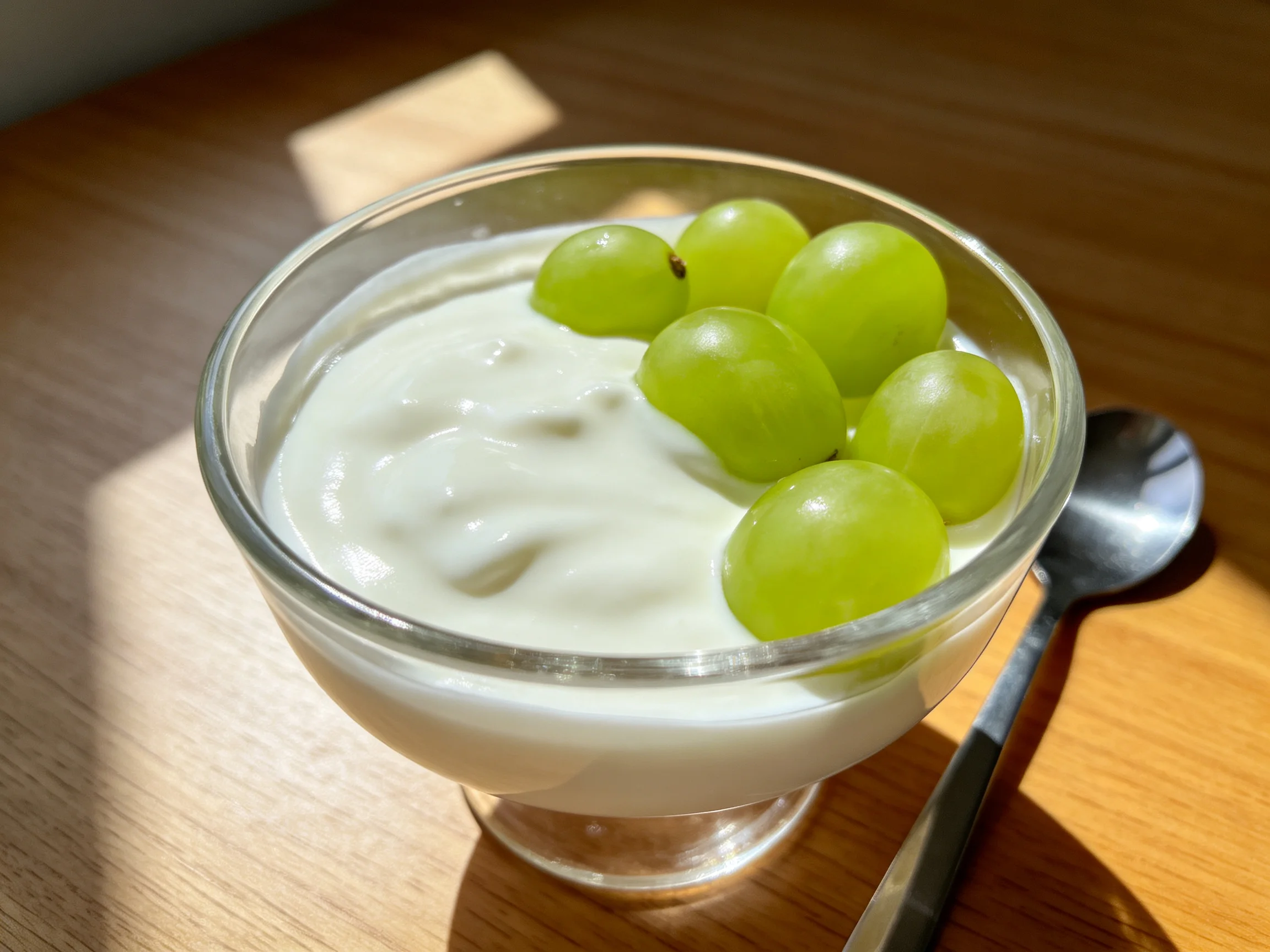 A glass bowl of creamy white yogurt topped with fresh green grapes