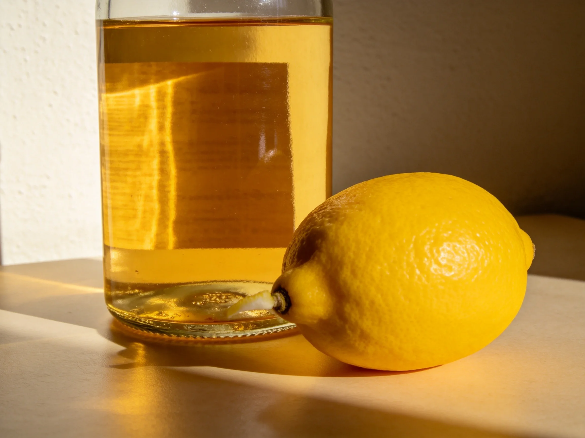 A glass jar filled with amber liquid next to a bright yellow lemon