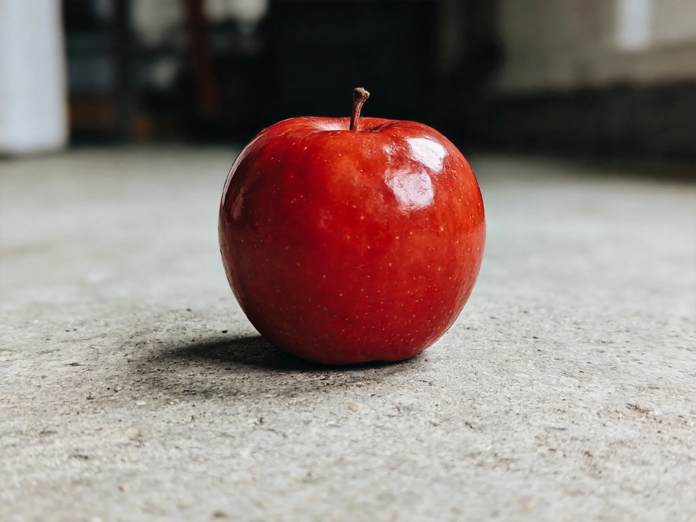 A glossy red apple rests on a smooth concrete surface