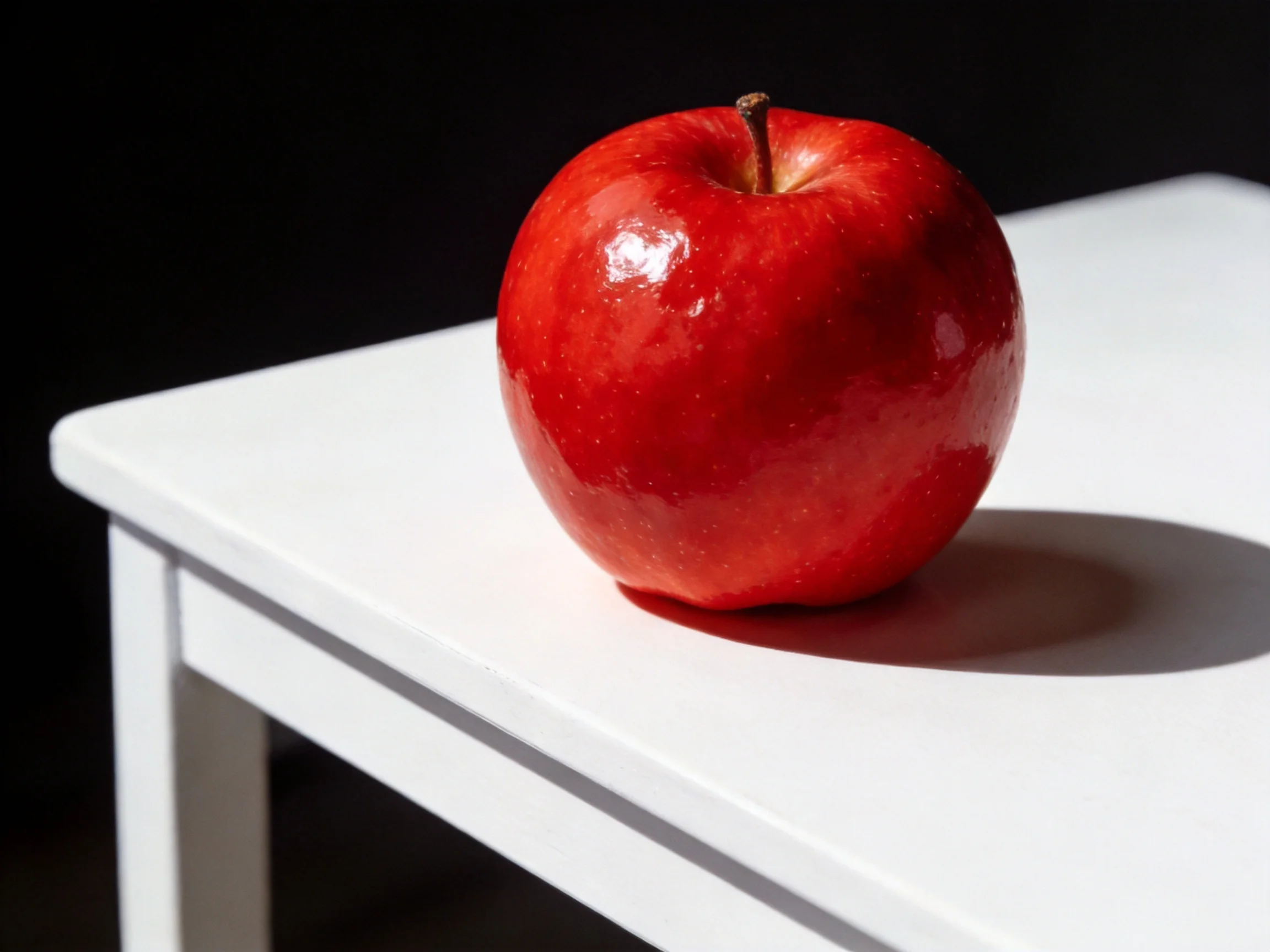 A glossy red apple sits atop a smooth white table