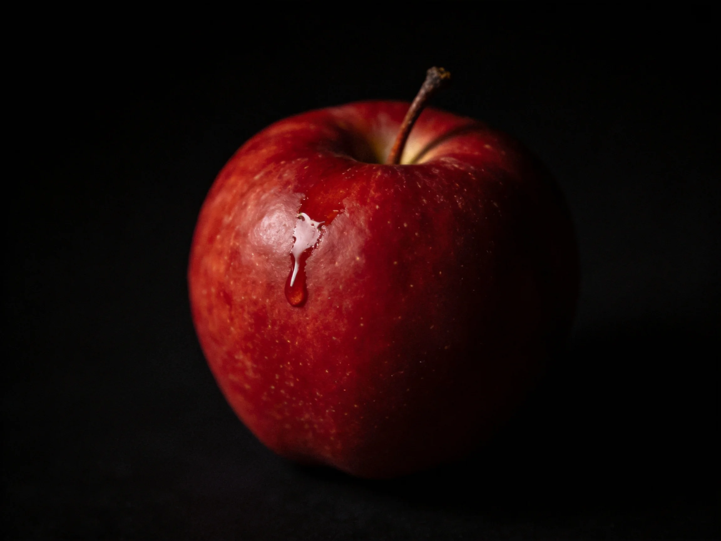 A glossy red apple with a juice droplet on a black background
