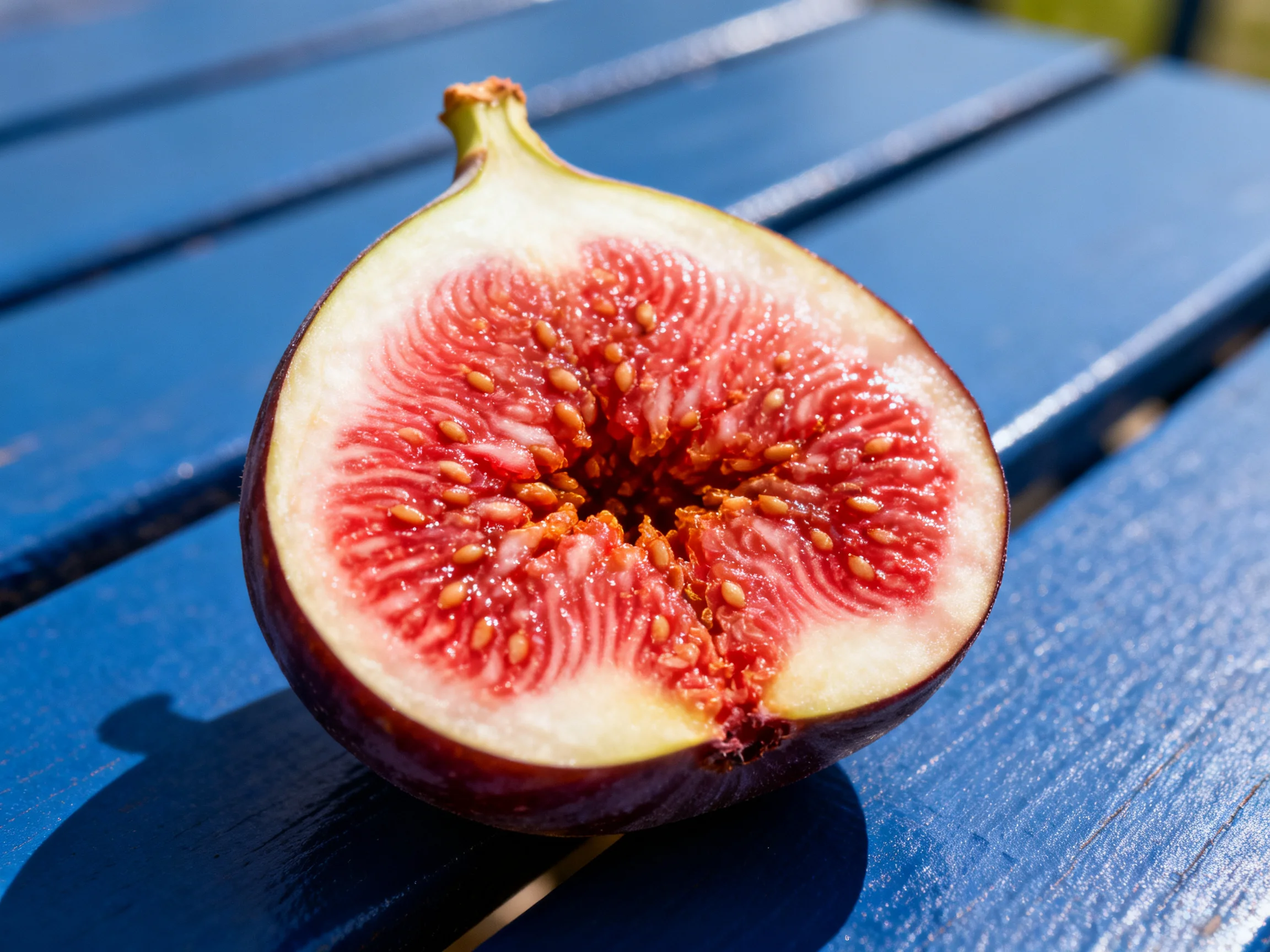 A halved fig with vibrant red flesh on a blue wooden bench