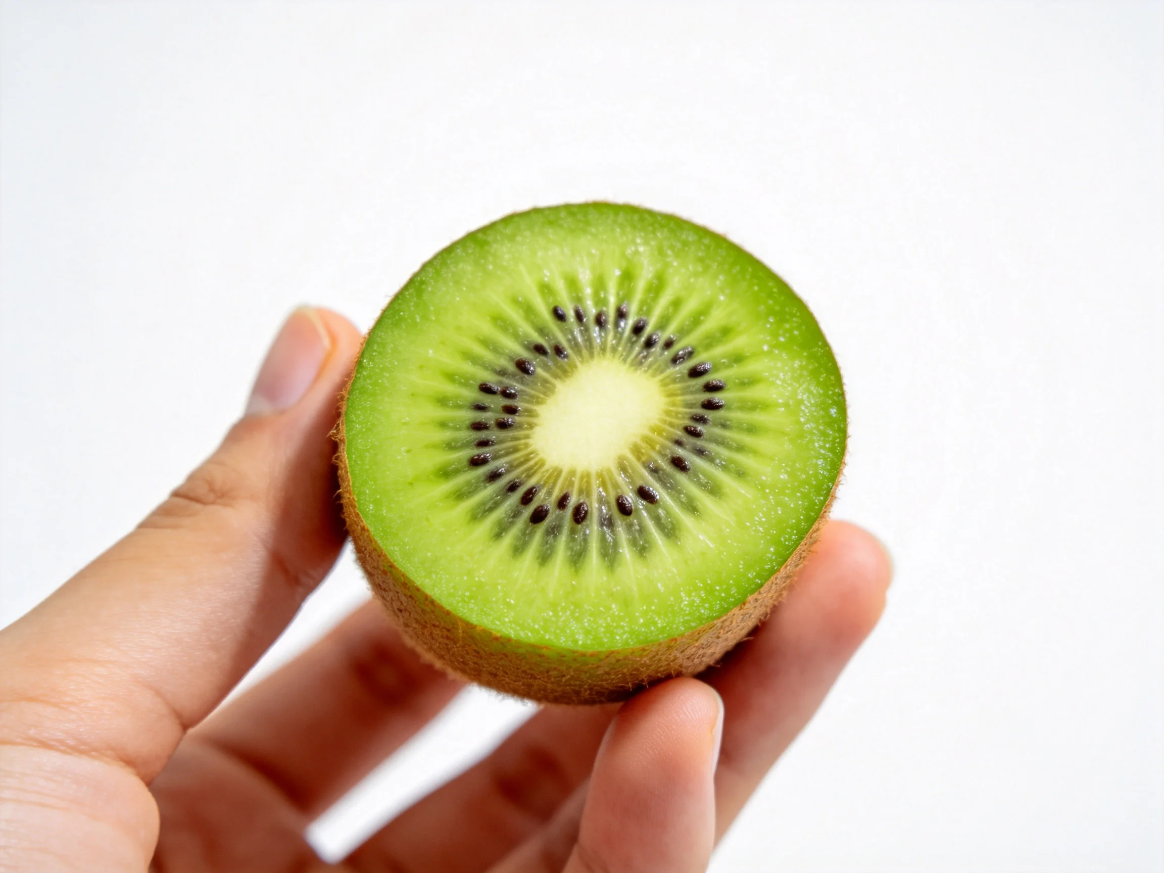 A halved green kiwi with black seeds held by fingers