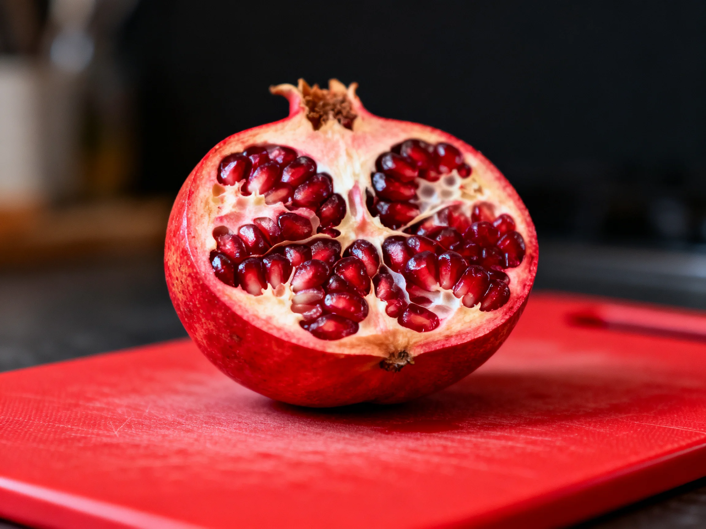 A halved pomegranate with vibrant red seeds on a bright red cutting board