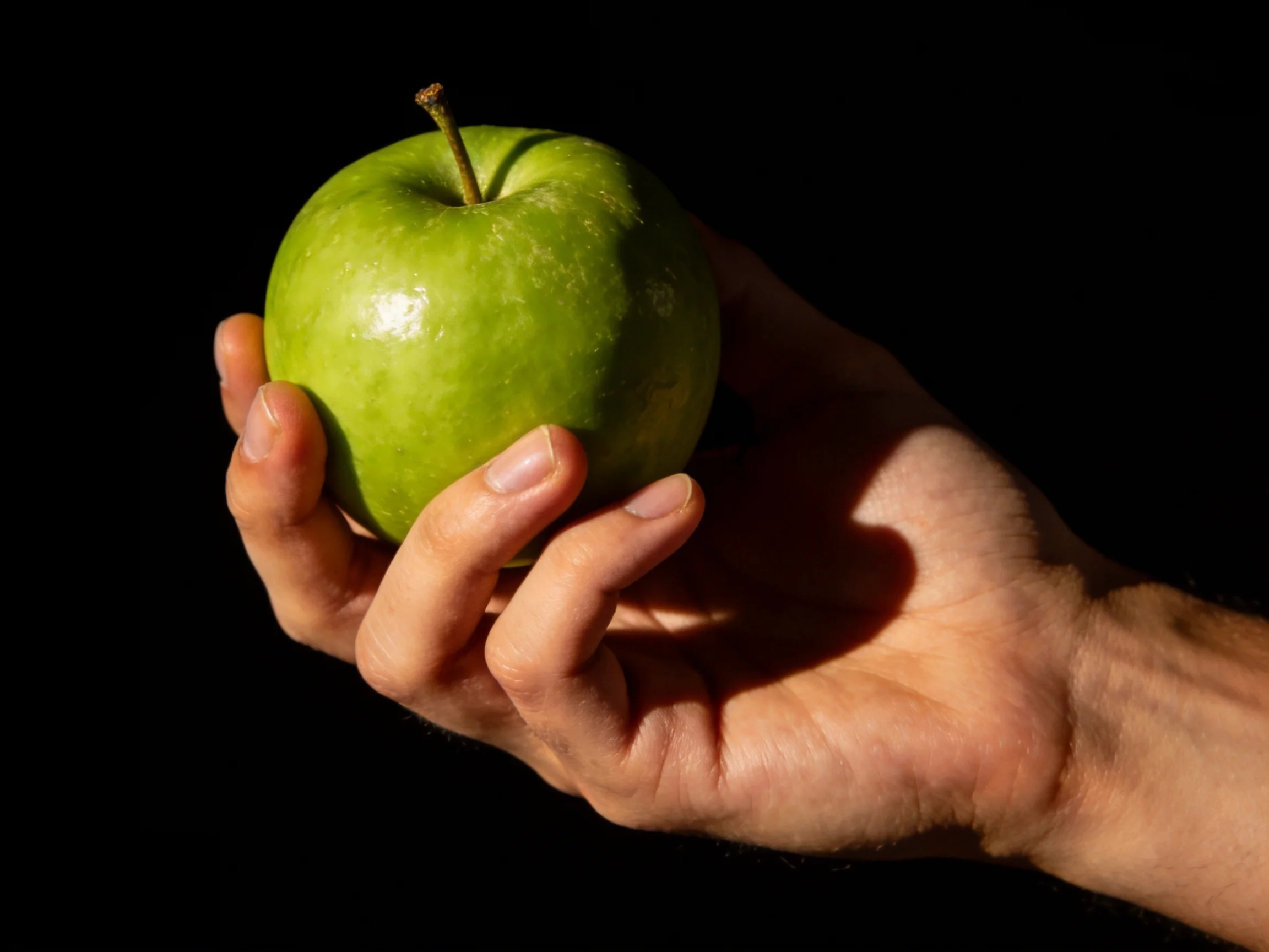 A hand cradles a vibrant green apple against a stark black backdrop