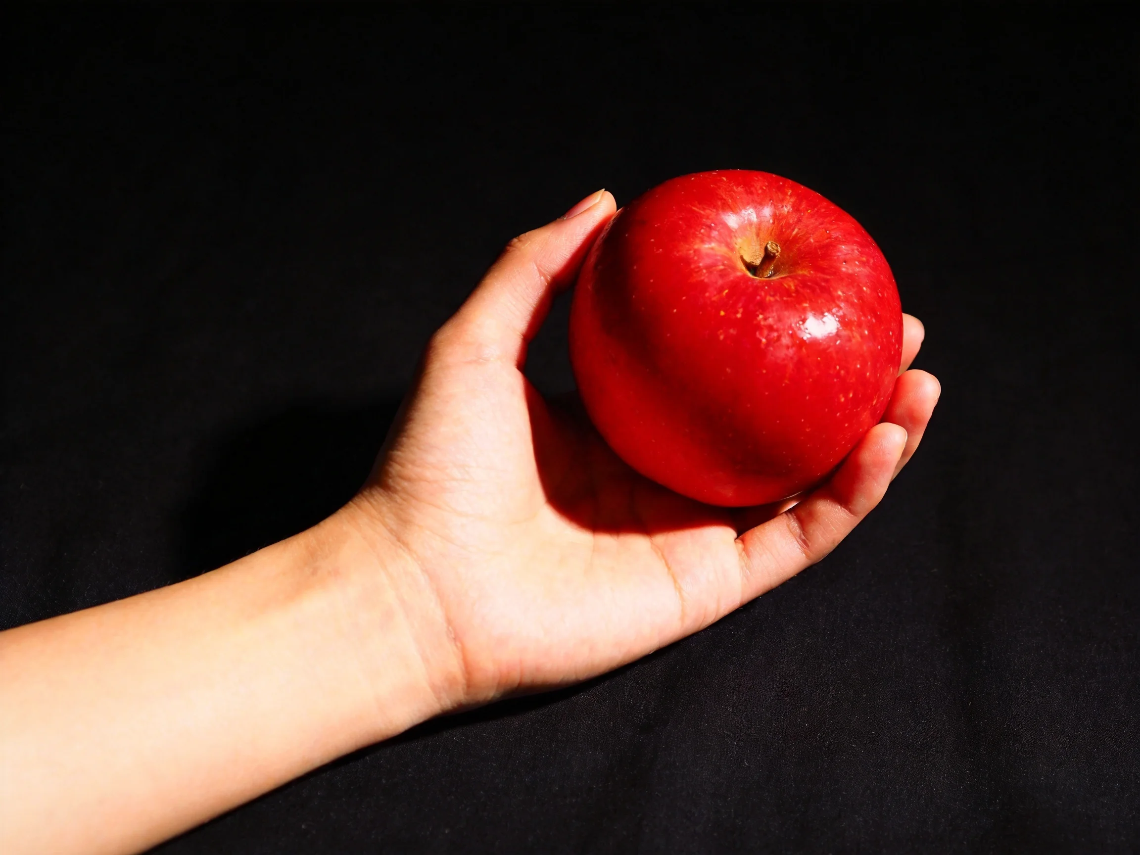 A hand holds a vibrant red apple against a solid black background