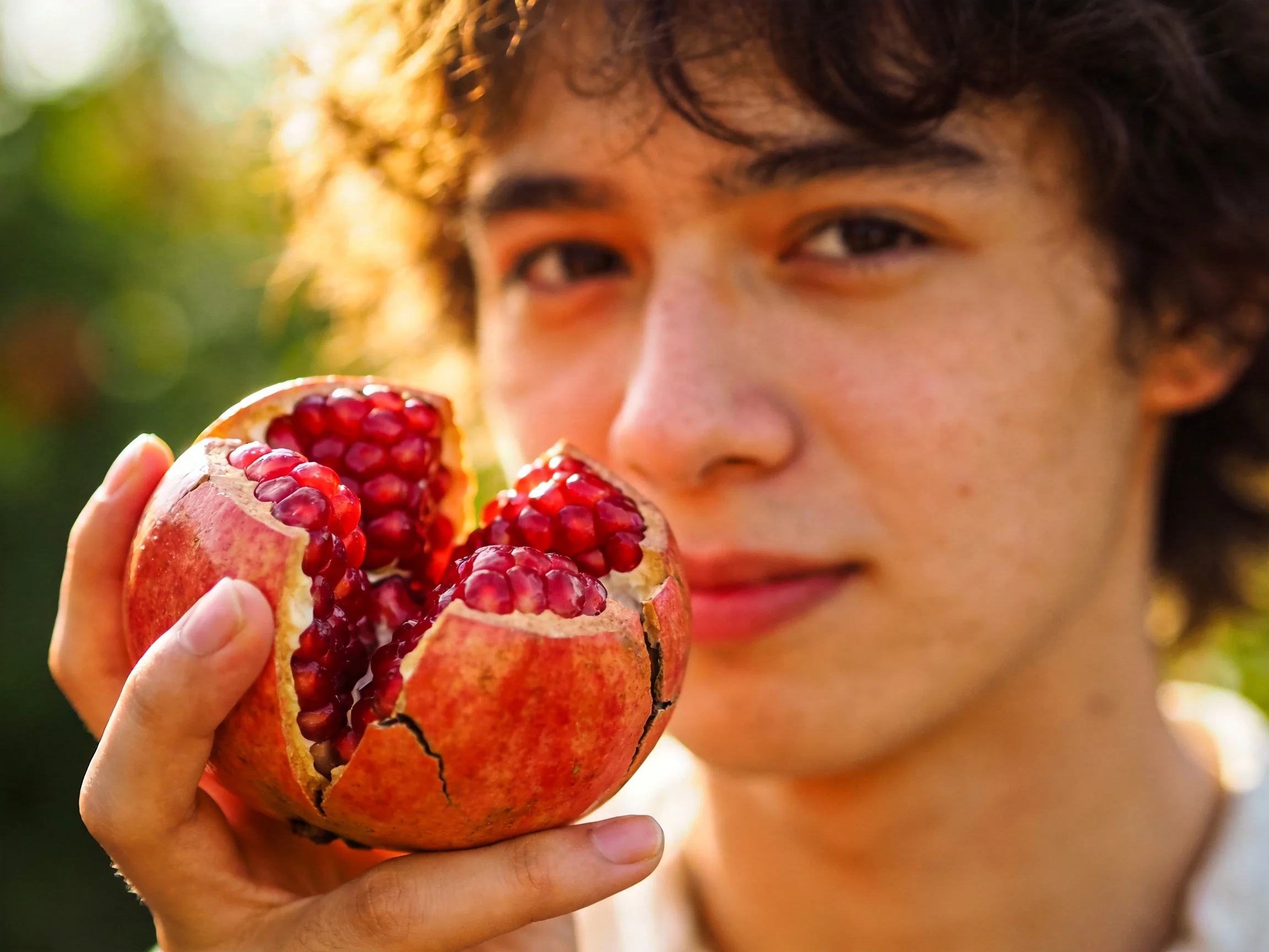 A person holding a cracked open, vibrant red pomegranate outdoors