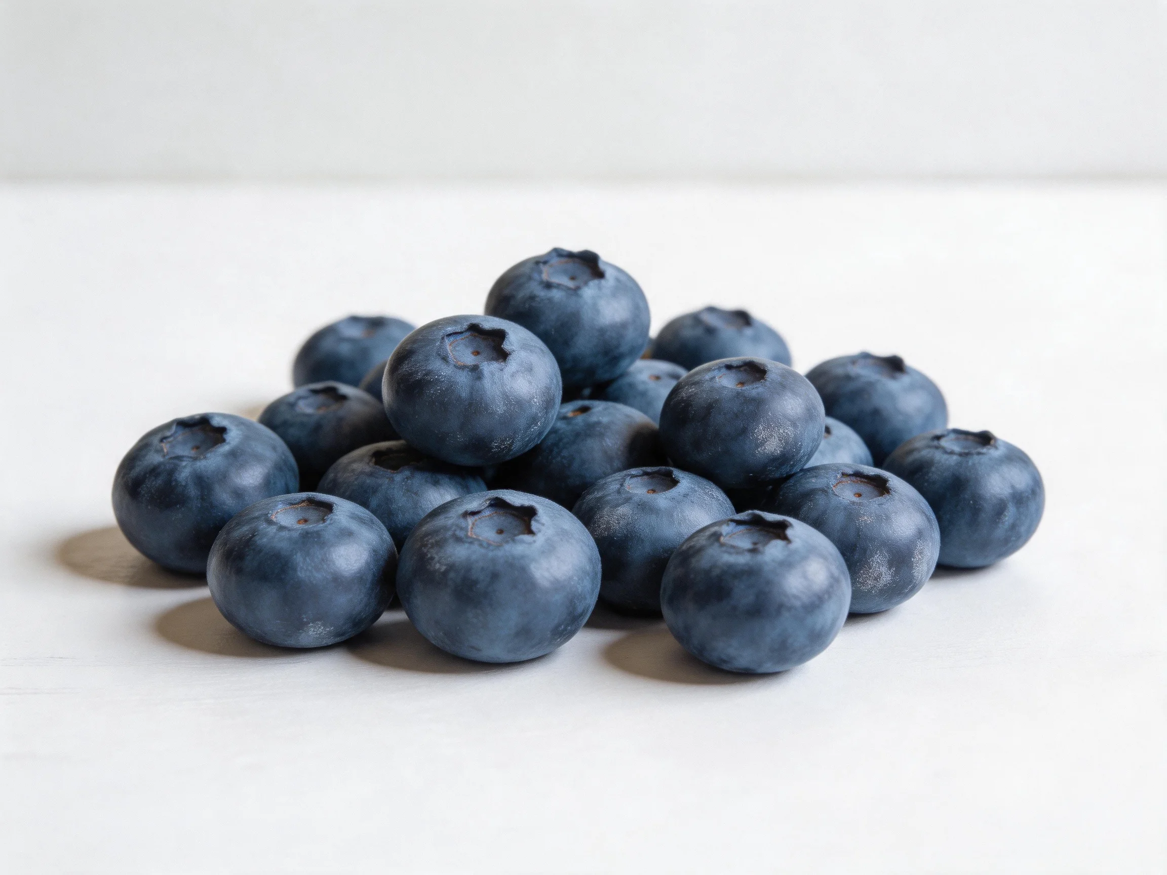 A pile of plump dark blueberries on a plain white surface